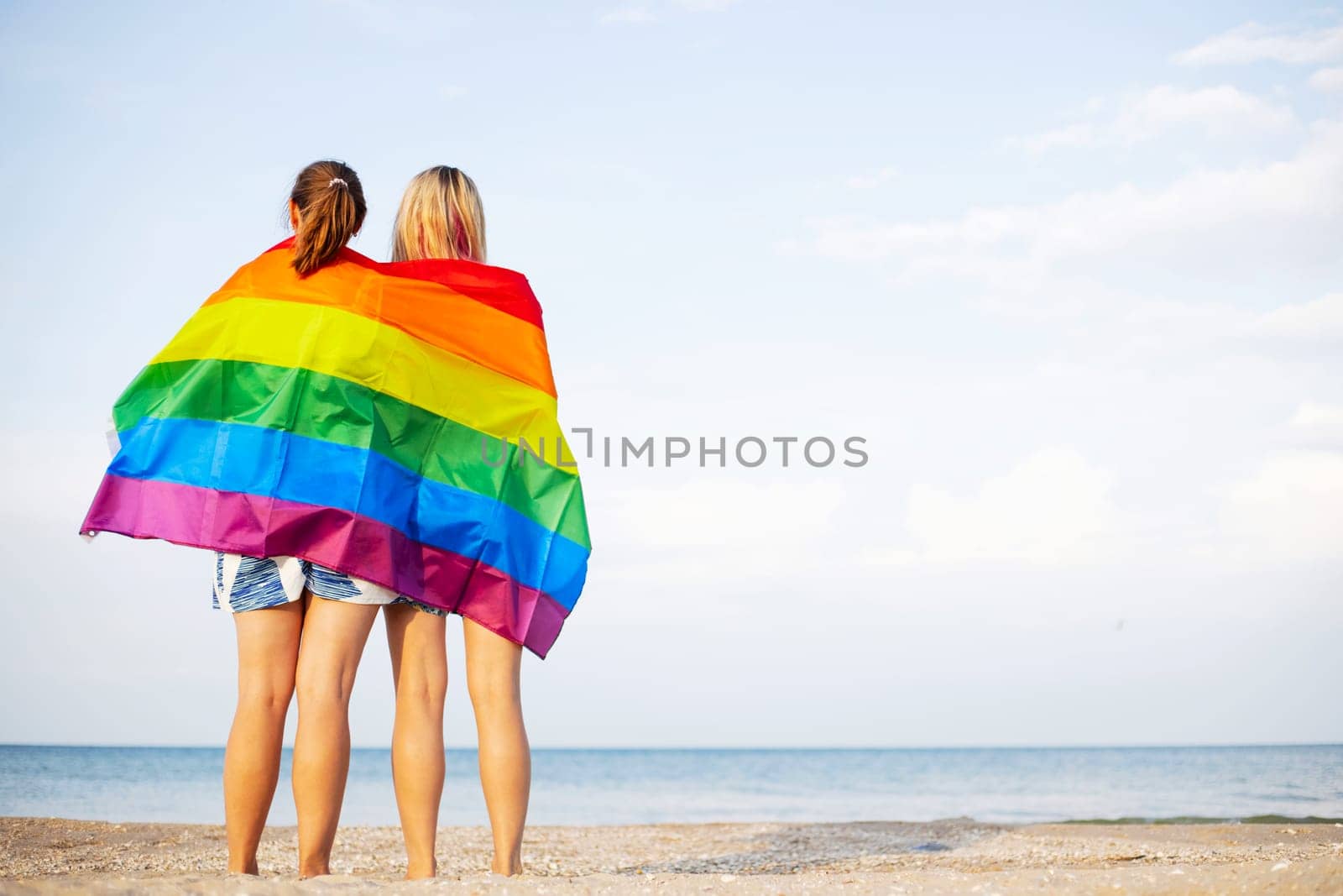 Lesbian couple holding lgbt flag and hugging outdoors. LGBT rainbow flag by andreyz