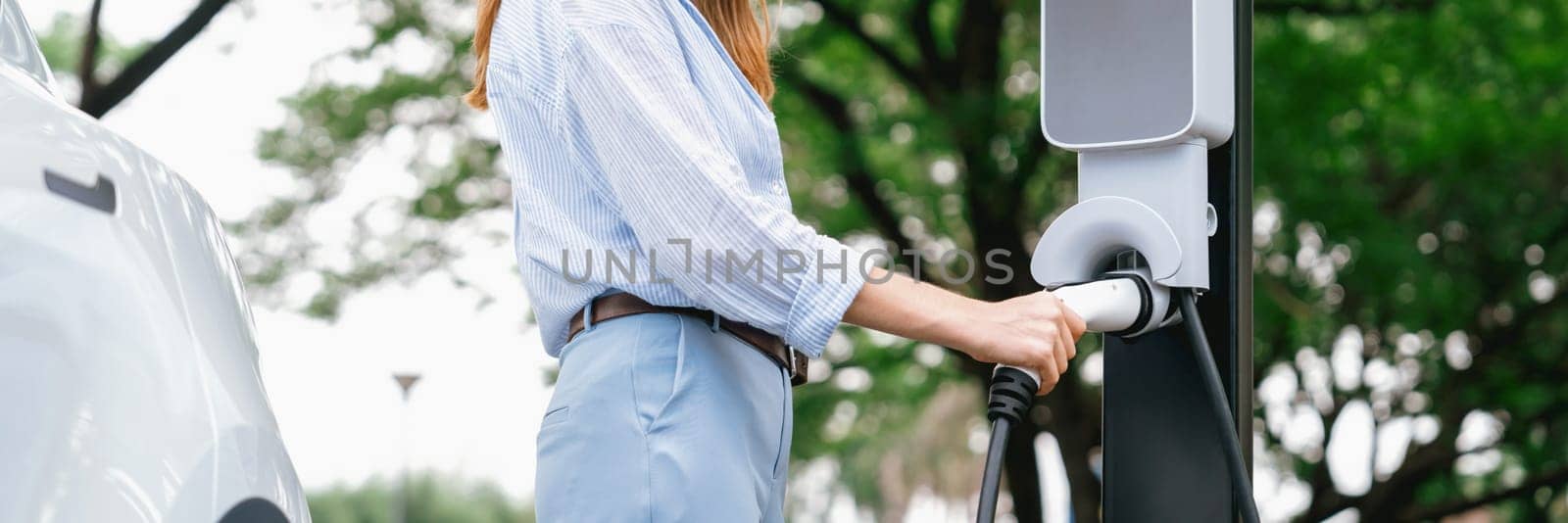 Young woman recharging battery for electric car during road trip. Exalt by biancoblue