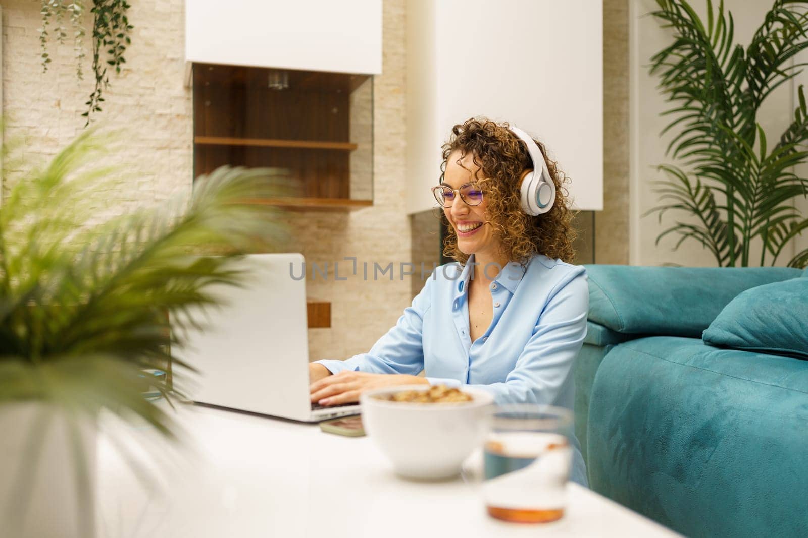 Smiling woman using laptop while doing remote work in living room by javiindy