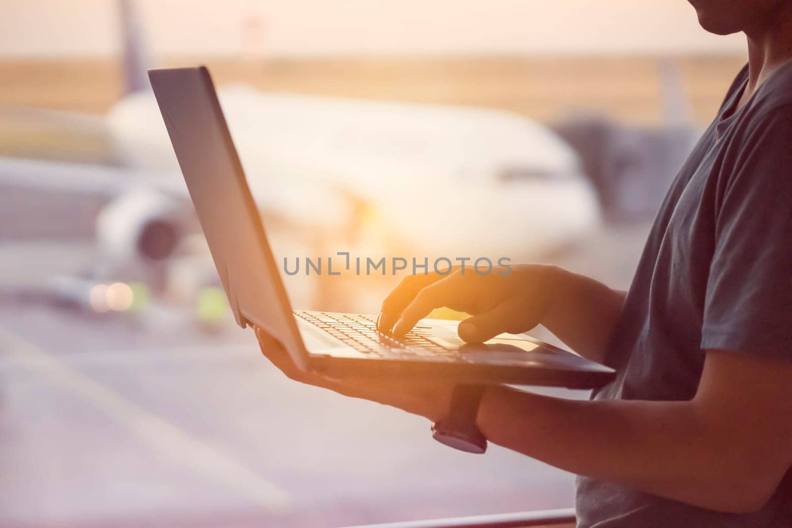 A young man is working on a laptop at the airport while waiting to board the plane. A man is engaged in business, buys tickets, studies and communicates via the Internet at sunset.