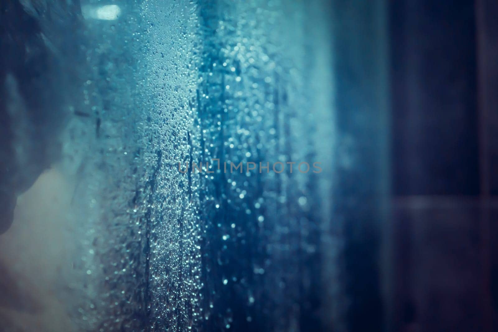 Large and small drops of water on the glass of a modern shower stall, a person takes a shower, a close-up view of the splashing water, a banner with copy space.