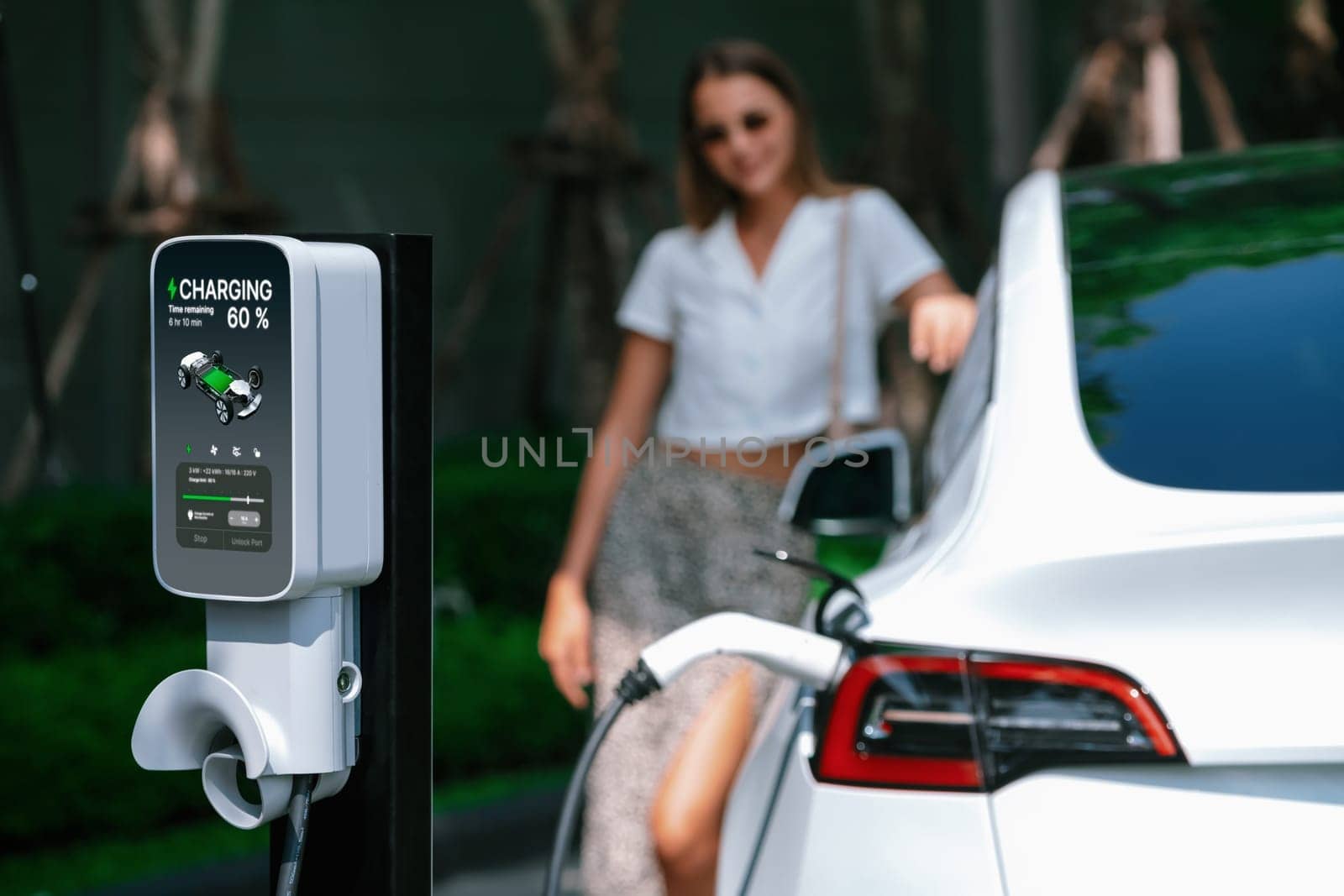 Young woman travel with EV electric car charging in green sustainable city outdoor garden in summer. Urban sustainability lifestyle by green clean rechargeable energy of electric BEV vehicle innards