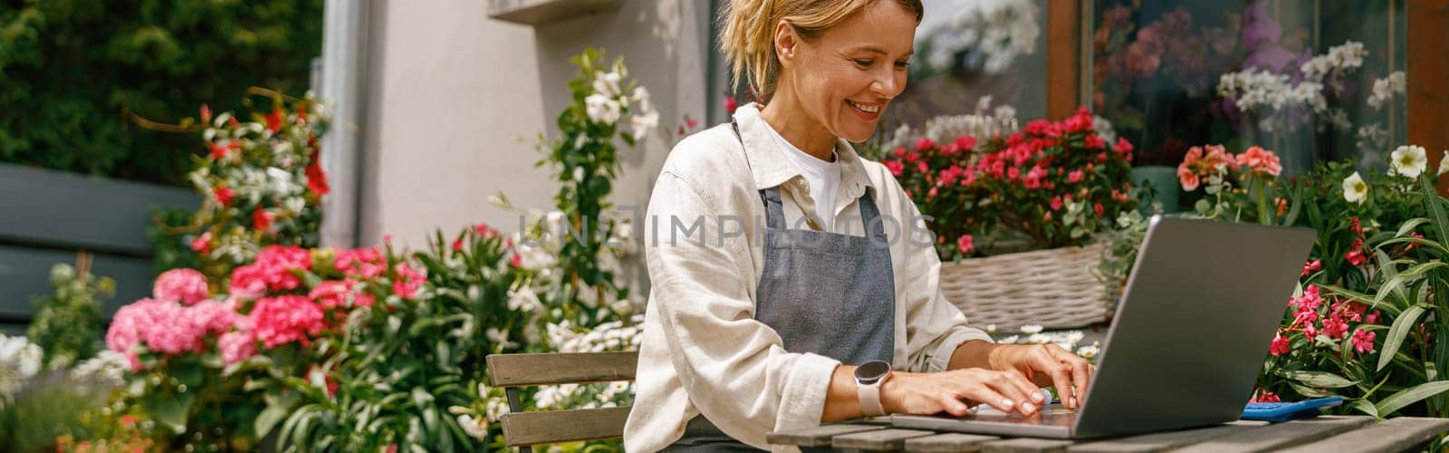 Small flower shop owner florist wearing apron working on laptop and taking online orders in store by Yaroslav_astakhov