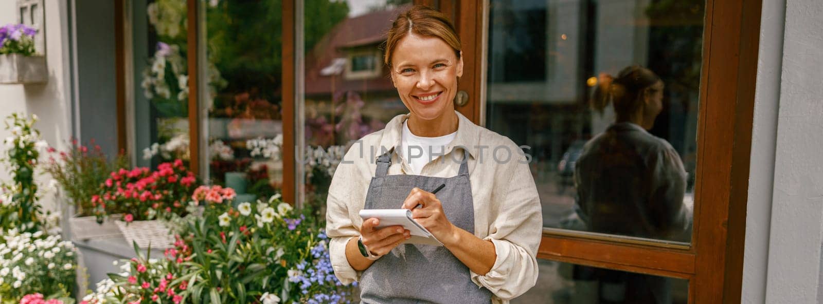 Woman florist writing orders and customer information in notebook at flower shop. High quality photo