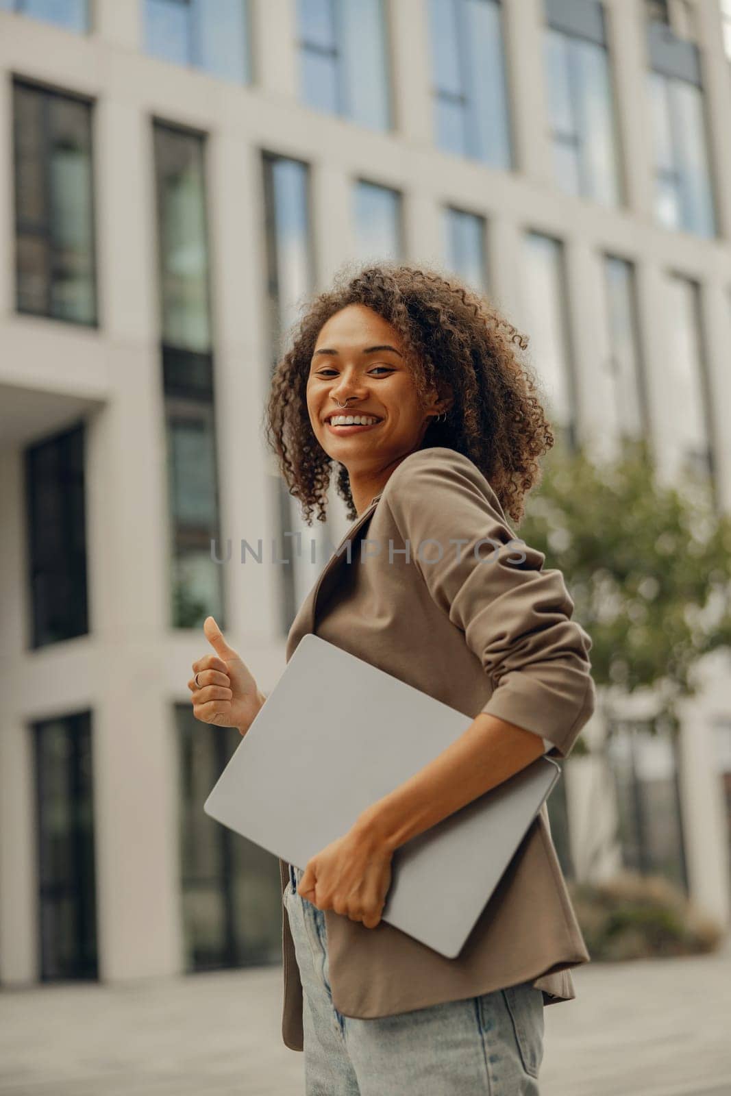 Stylish female manager standing with laptop on office building background during break time