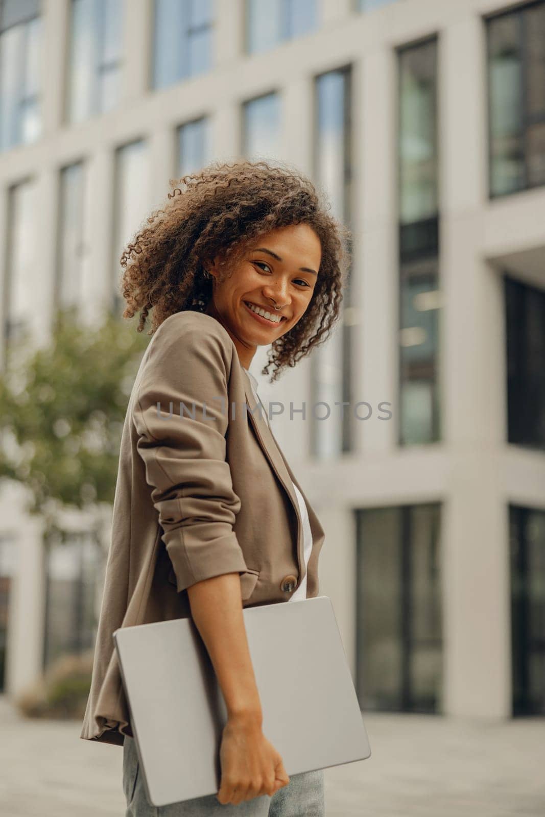 Stylish female manager standing with laptop on office building background during break time