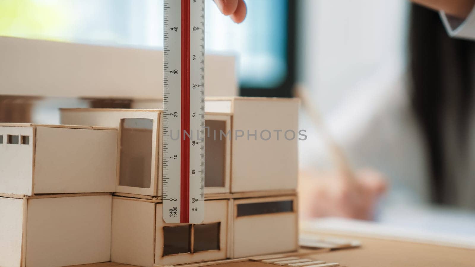 Closeup image of skilled professional engineer hand using ruler measures house model on table with blurred background. Creative design, architect design, architectural equipment concept. Immaculate.