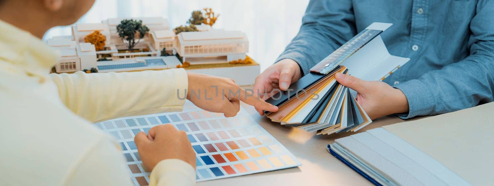 Interior designer team present color selection to project manager with color swatches and architectural model on meeting table. Creative working and design concept. Focus on hand. Variegated.