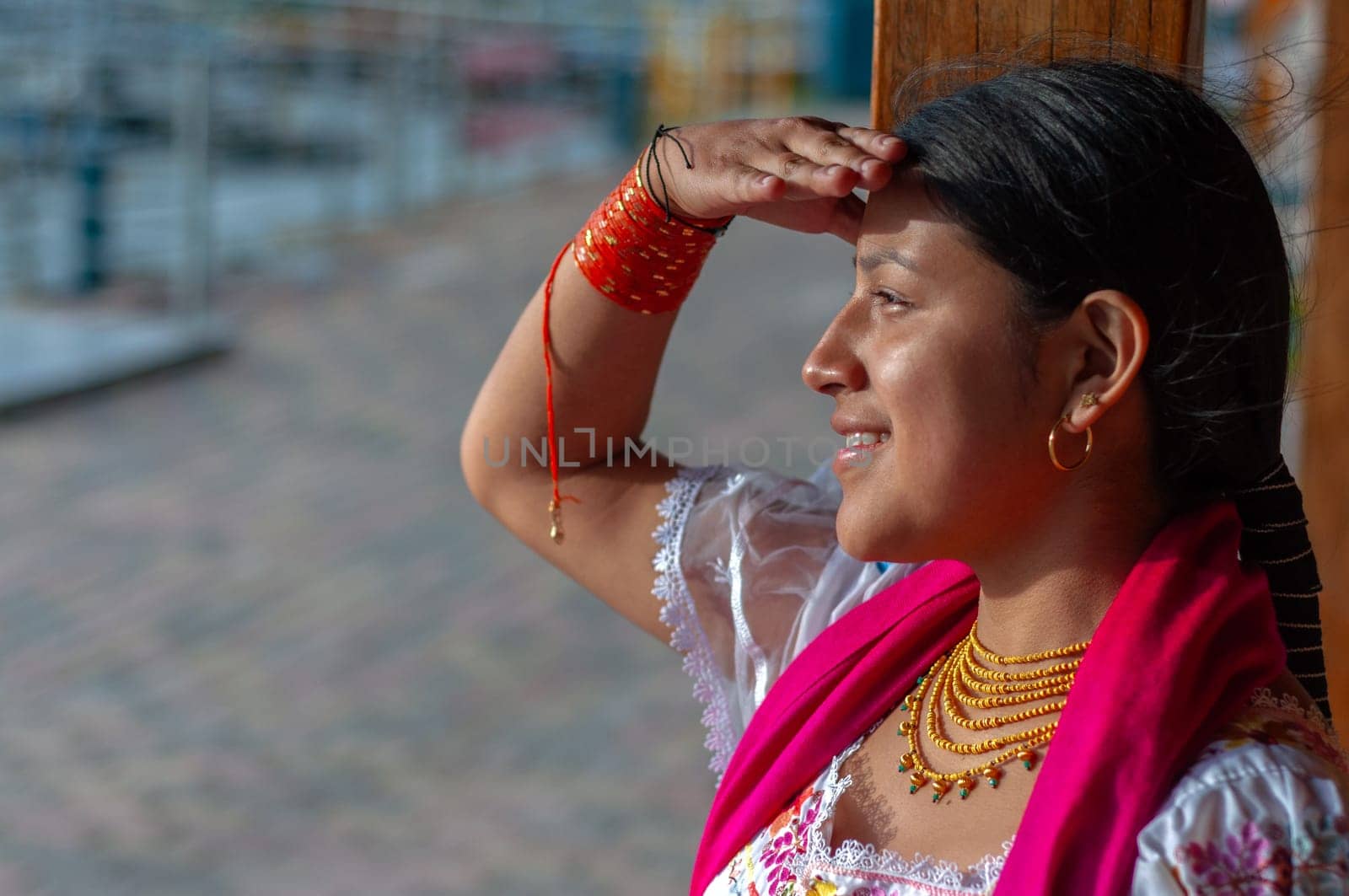 copy space of a beautiful indigenous woman with traditional dress and gold jewelry with her hand on her forehead looking towards the horizon with a face of enthusiasm and happiness. High quality photo