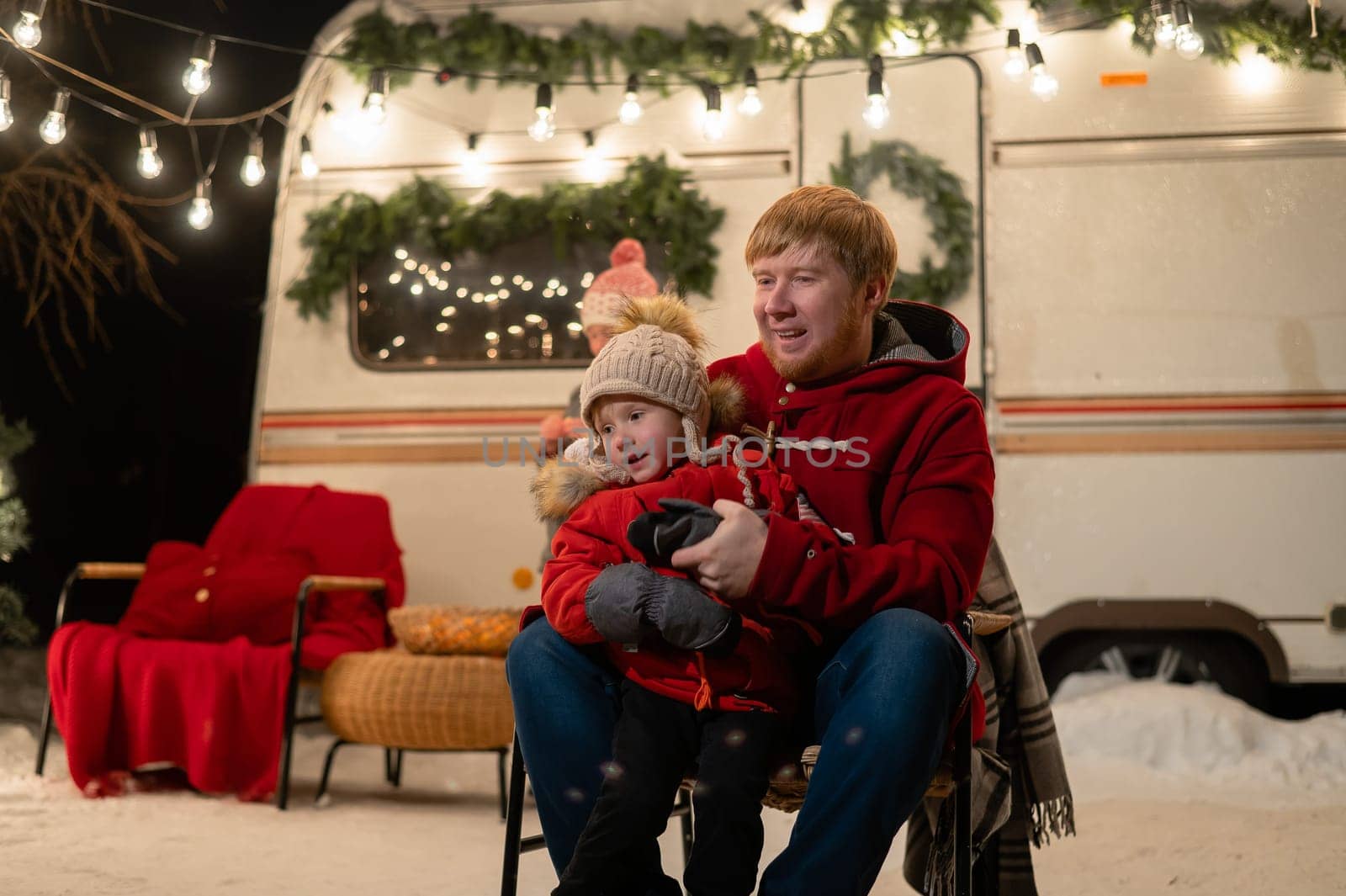 Caucasian red-haired man with a boy in his arms at the mobile home. Father and son celebrate Christmas on a trip
