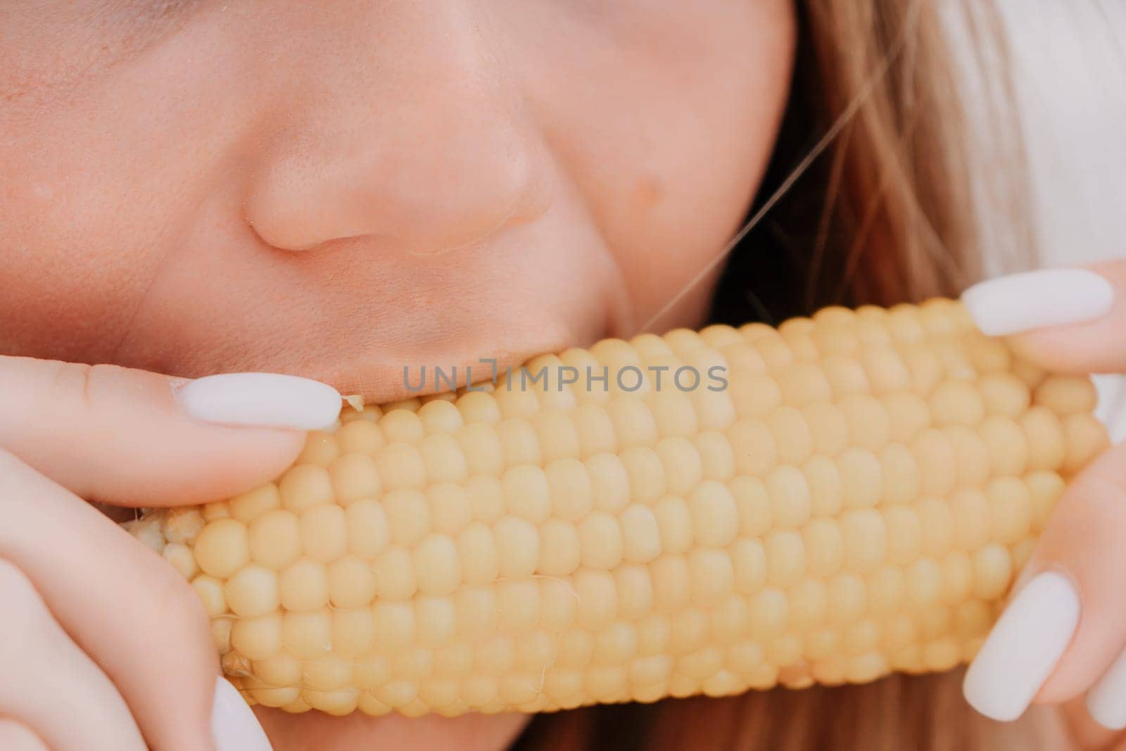 Woman eats corn on beach. Woman's hands hold delicious juicy grilled corn. A natural and healthy snack at the beach. Close-up. by panophotograph