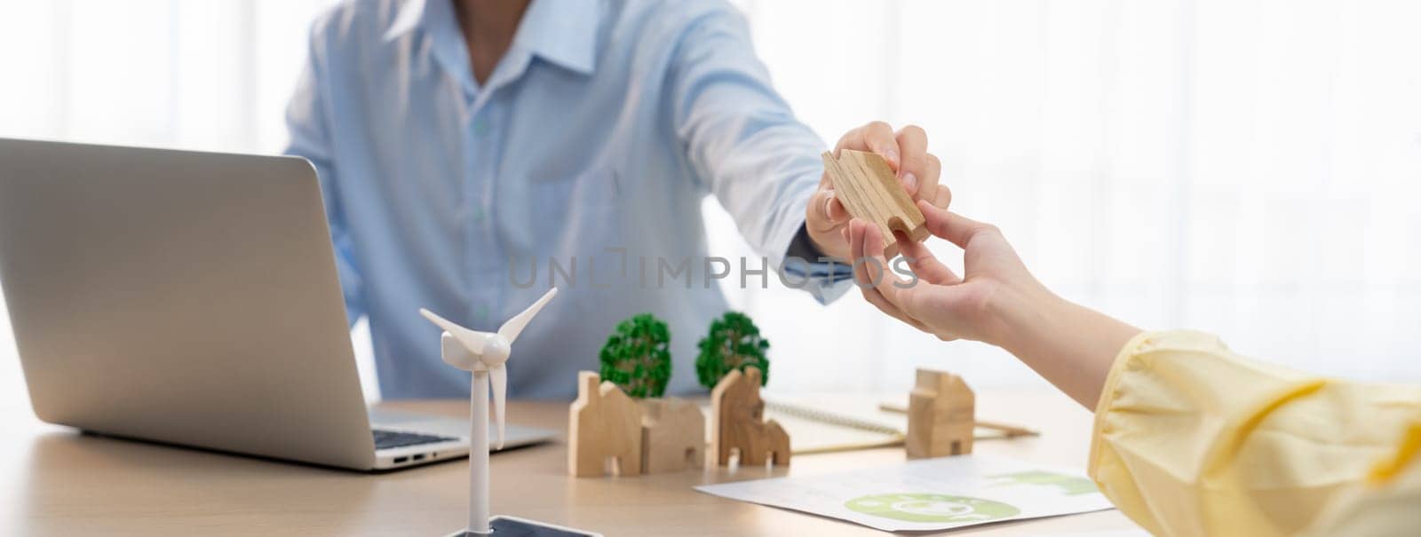 Two business people talking about eco city at green business meeting on meeting table with windmill represented renewable energy, wooden house block and tree model represent green city. Delineation.