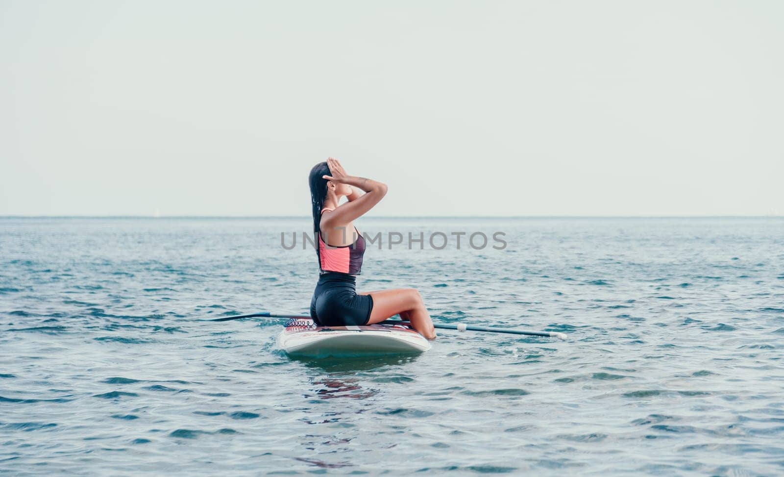Sea woman sup. Silhouette of happy young woman in pink bikini, surfing on SUP board, confident paddling through water surface. Idyllic sunset. Active lifestyle at sea or river. by panophotograph