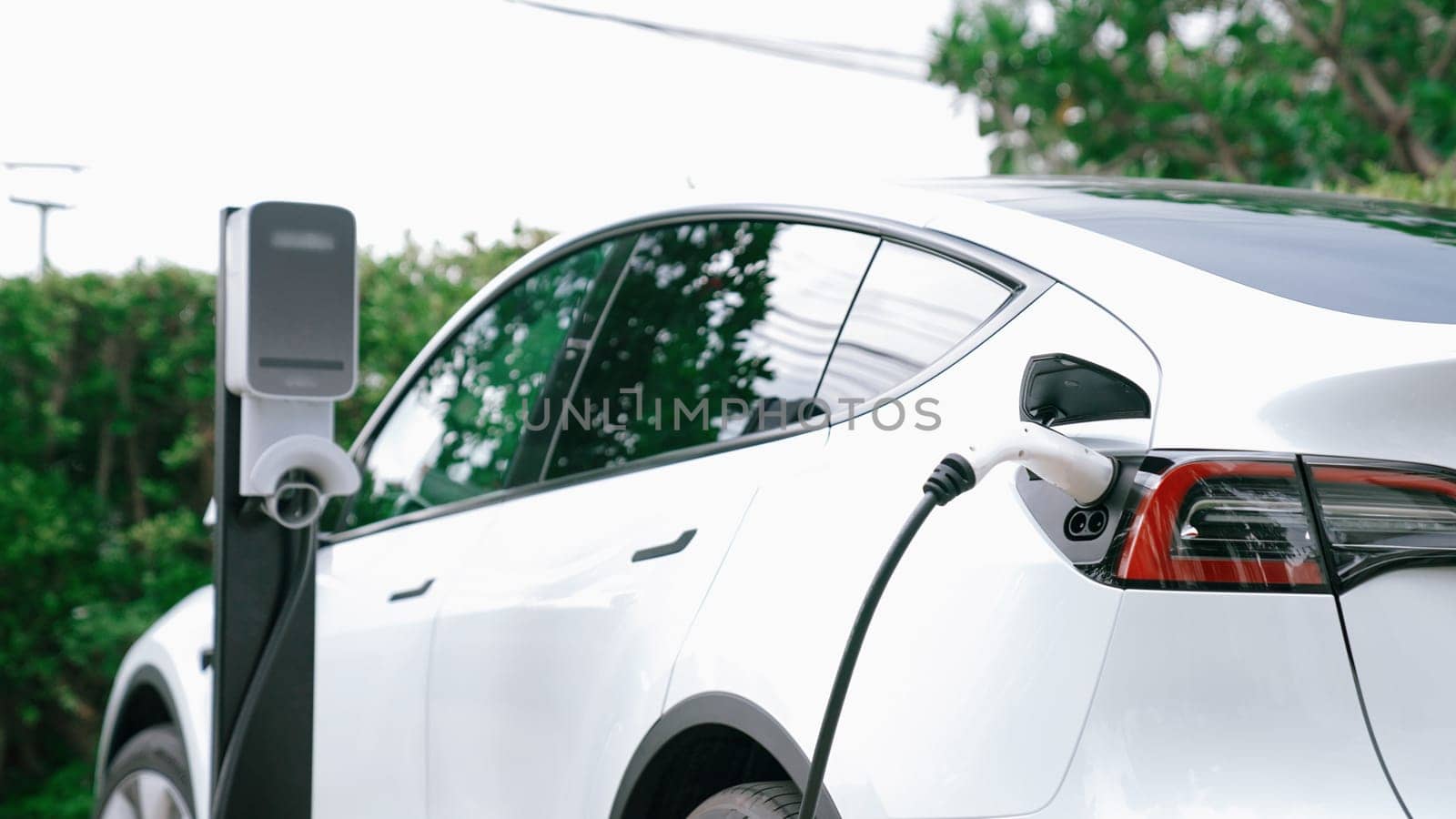 EV electric car recharge battery at parking lot in green city park. Synchronos by biancoblue