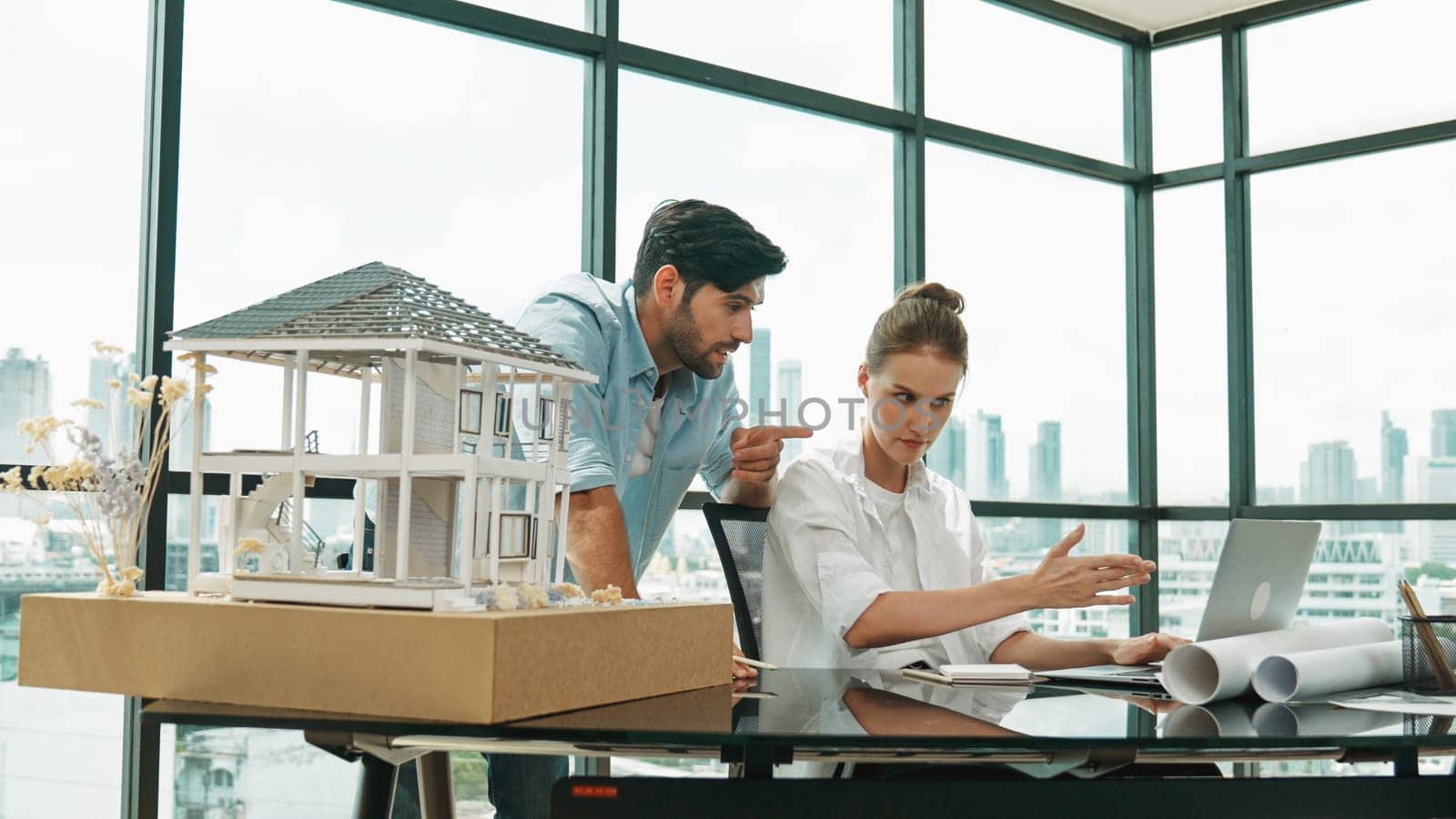 Smart architect engineer inspect house model while colleague using laptop analysis data. Professional designer team working together to design house model construction at modern office. Tracery