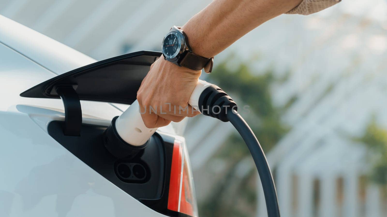 Closeup hand put EV charger to recharge electric car's battery from charging station in city commercial parking lot. Rechargeable EV car for sustainable environmental friendly urban travel. Expedient