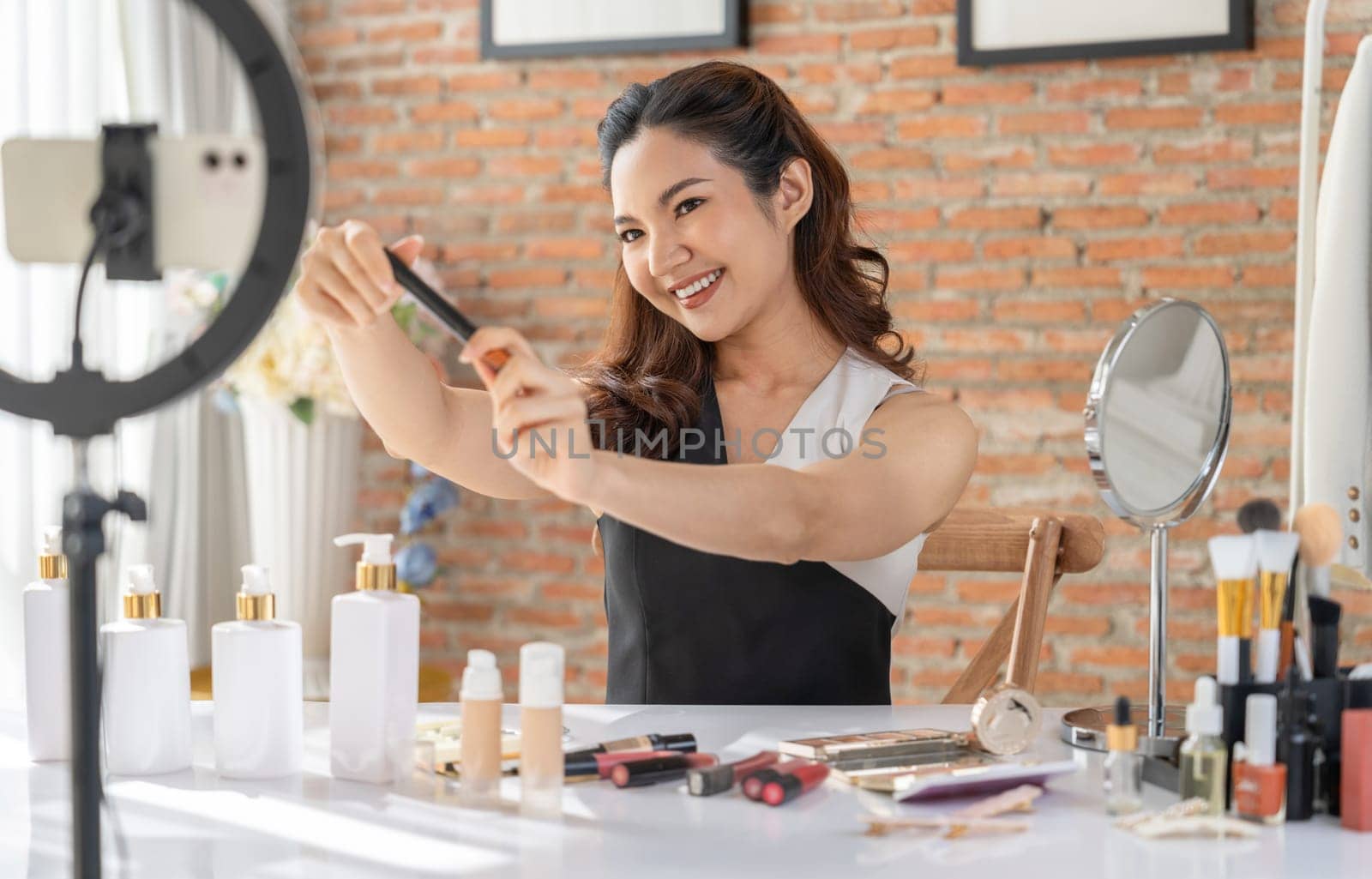 Woman influencer shoot live streaming vlog video review makeup uttermost social media or blog. Happy young girl with cosmetics studio lighting for marketing recording session broadcasting online.