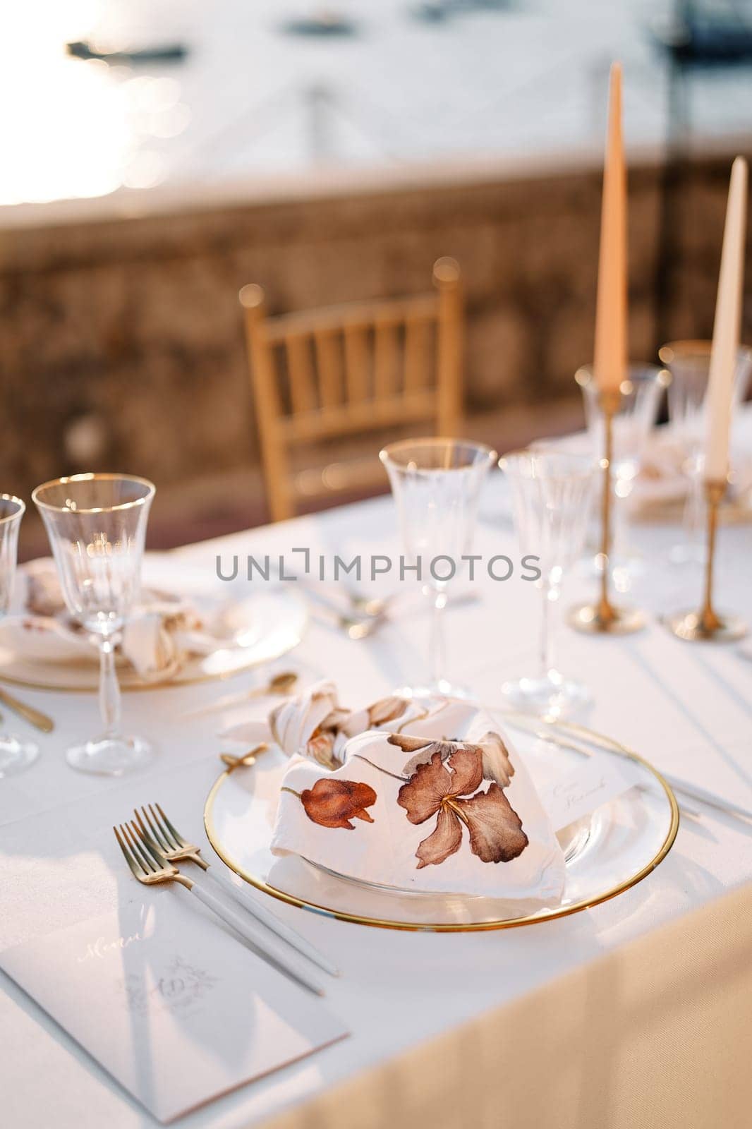 Festive menu lies near the cutlery next to a plate with a knotted napkin on a set table by Nadtochiy