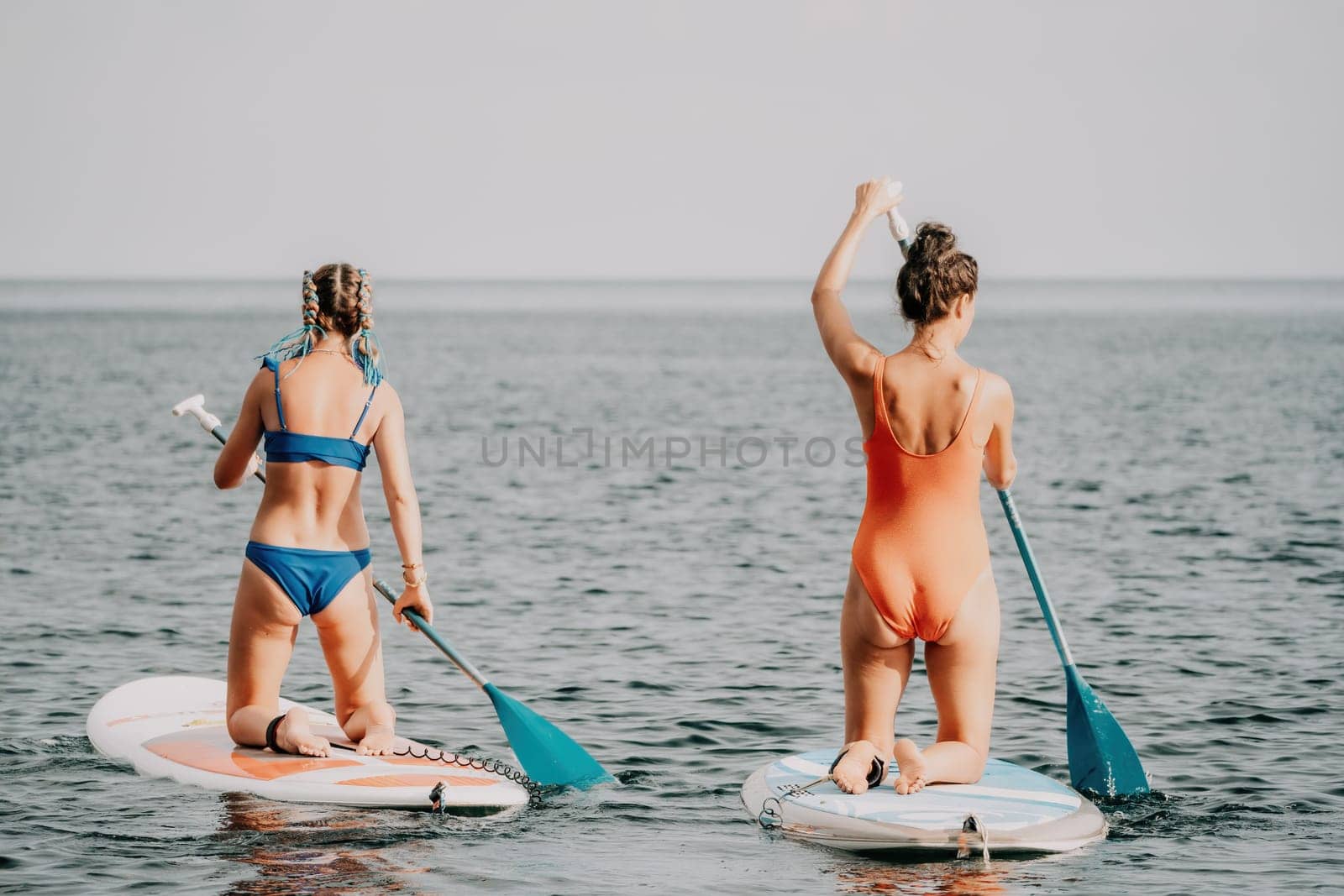 Woman sup yoga. Middle age sporty woman practising yoga pilates on paddle sup surfboard. Female stretching doing workout on sea water. Modern individual hipster outdoor summer sport activity