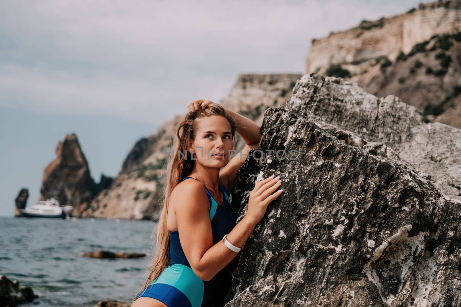 Woman travel sea. Happy tourist in blue swimwear takes a photo outdoors to capture memories. woman traveling and enjoying her surroundings on the beach, with volcanic mountains in the background. by panophotograph