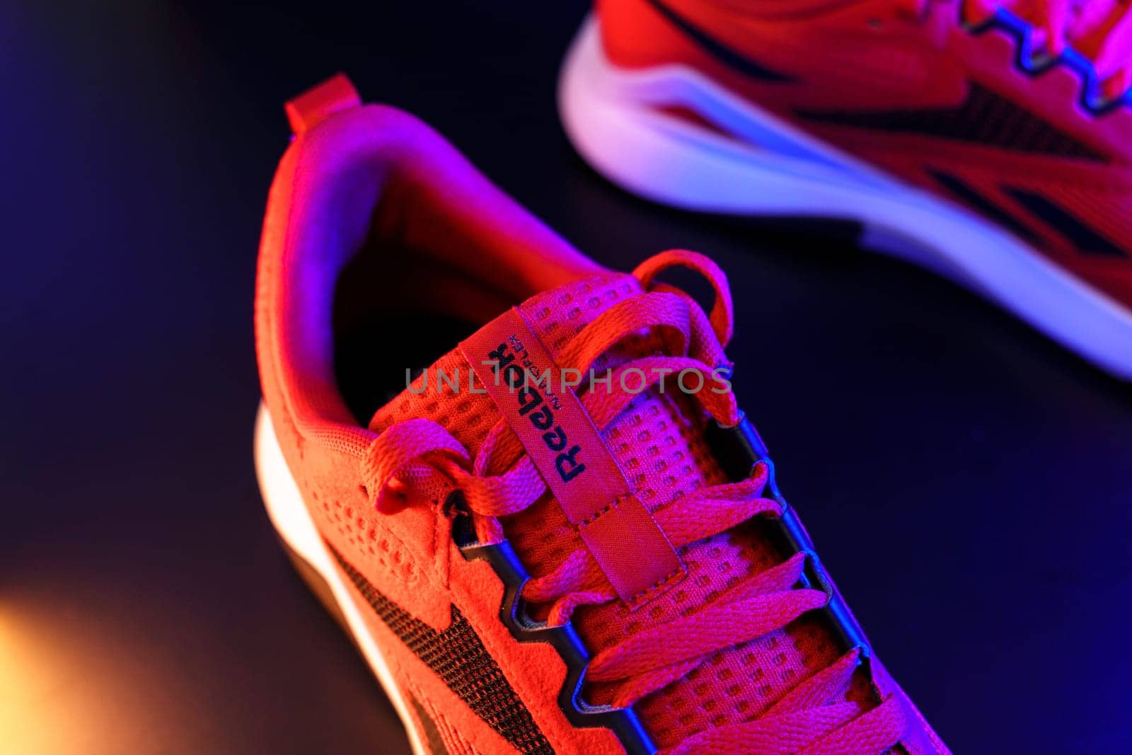 Tyumen, Russia-August 03, 2023: Red Reebok logo model Nanoflex sneakers, running shoes. Multicolored light. Selective focus by darksoul72