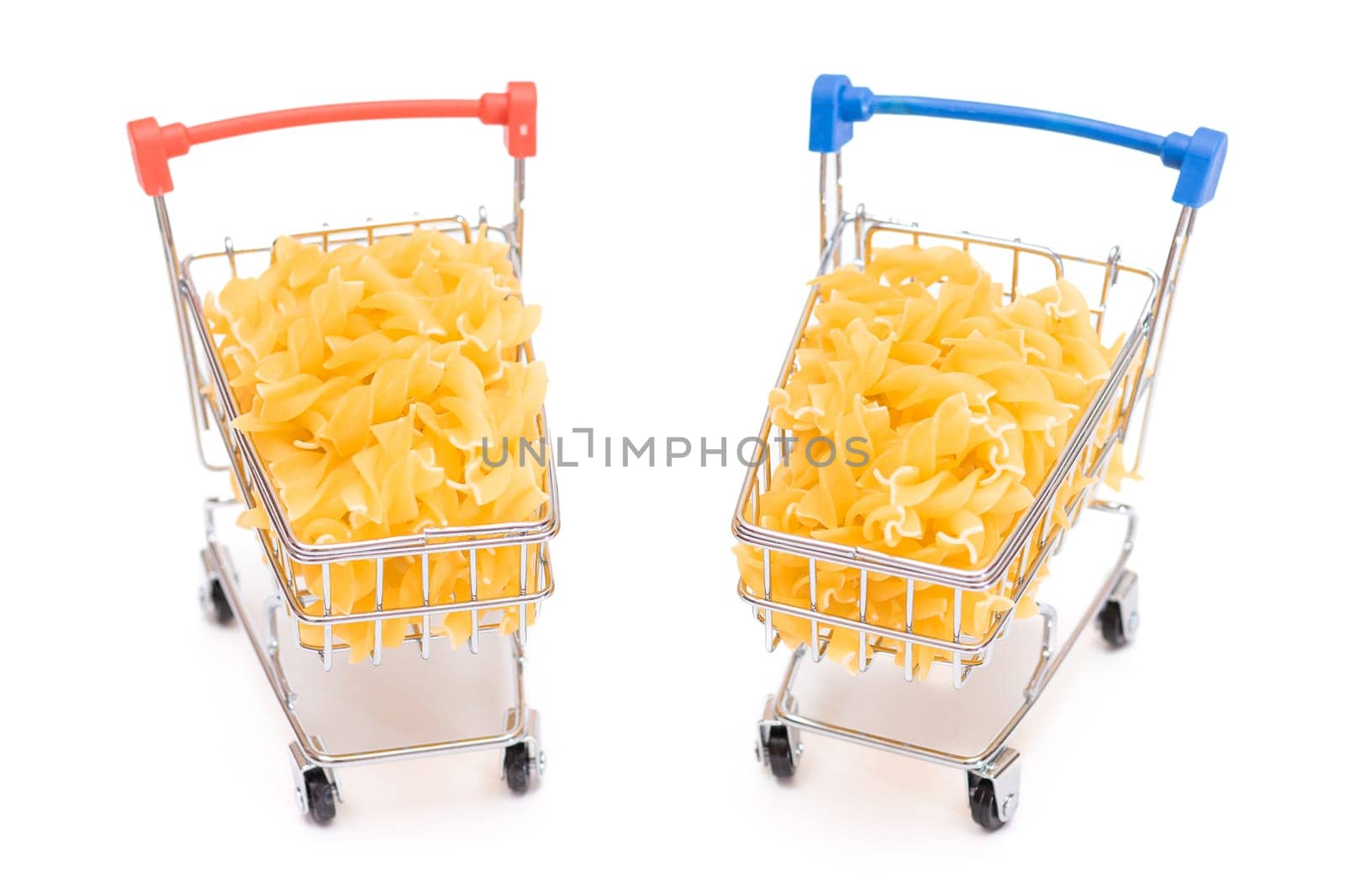 Uncooked Fusilli Pasta in Two Small Shopping Carts Isolated on White Background. A Crisis: Buying Cheap Food. Classic Dry Spiral Macaroni. Italian Culture and Cuisine. Raw Pasta - Isolation