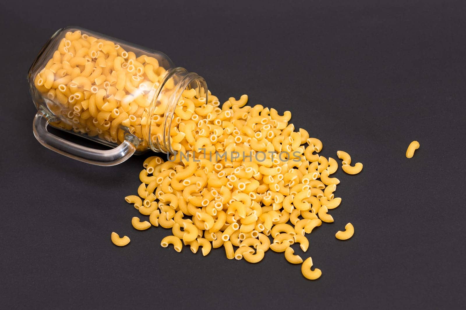 Uncooked Chifferi Rigati Pasta in Glass Jar on Black Background. Fat and Unhealthy Food. Scattered Classic Dry Macaroni. Italian Culture and Cuisine. Raw Pasta