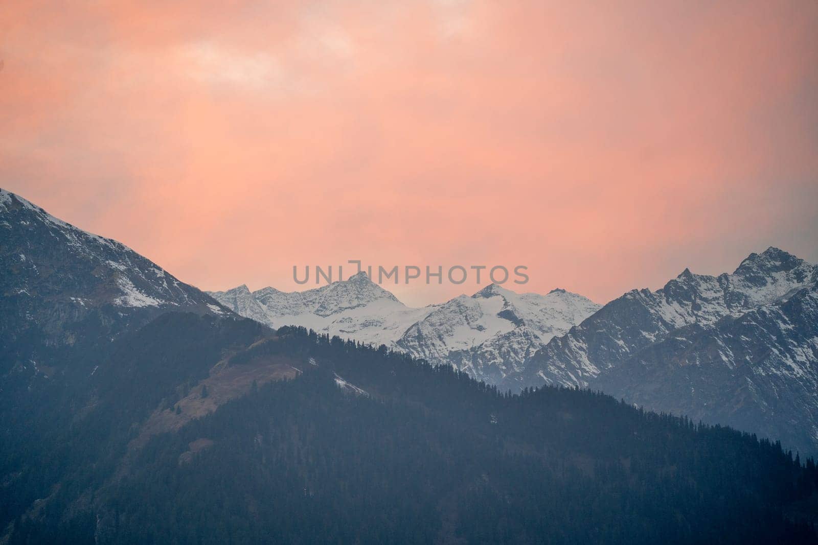 red orange dusk dawn colors over snow covered himalaya mountains and fluffy clouds showing hill stations in jhibbi kullu manali India