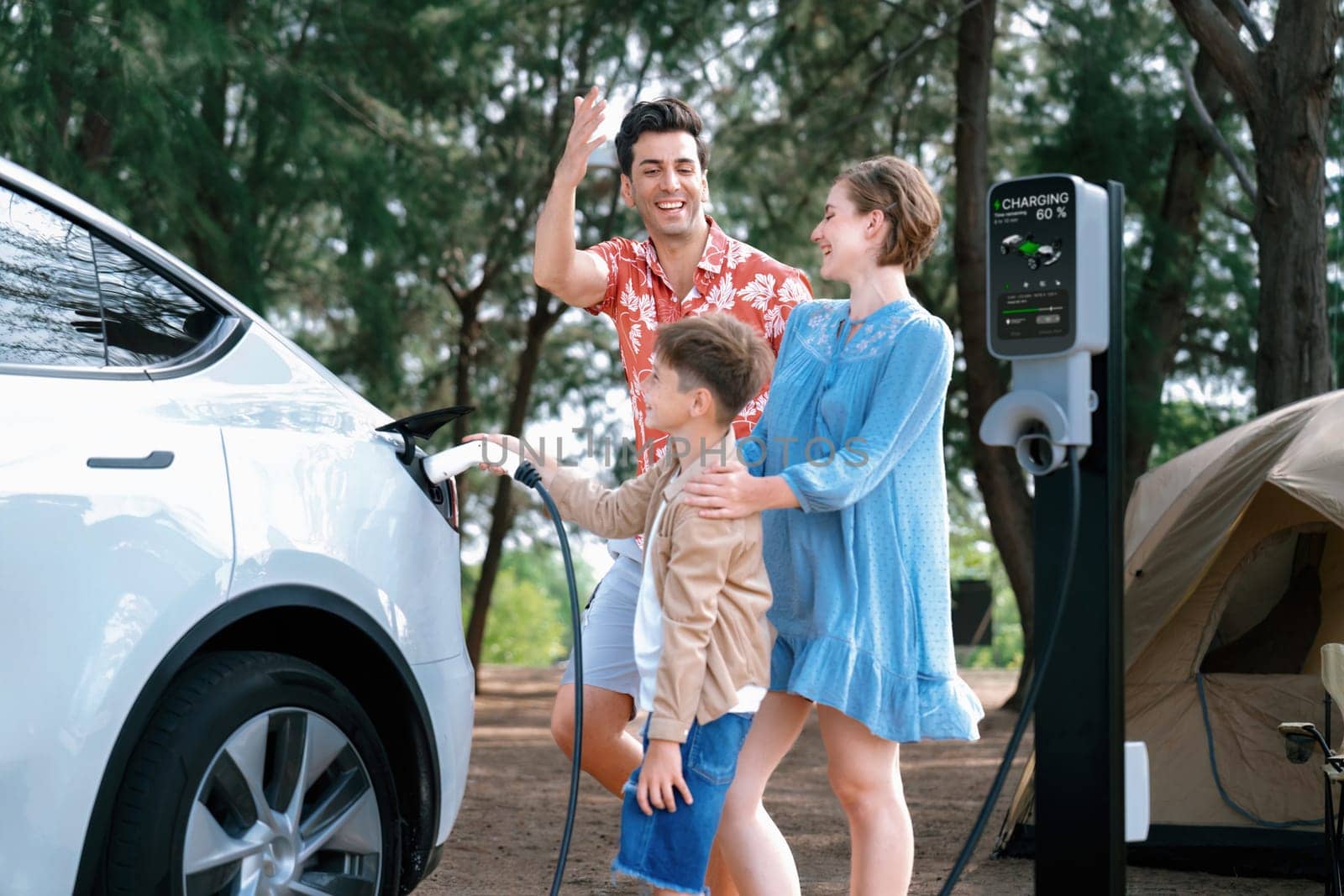 Outdoor adventure and family vacation camping in nature travel by eco friendly car for sustainable future. Lovely family recharge EV car with EV charging station in campsite. Perpetual