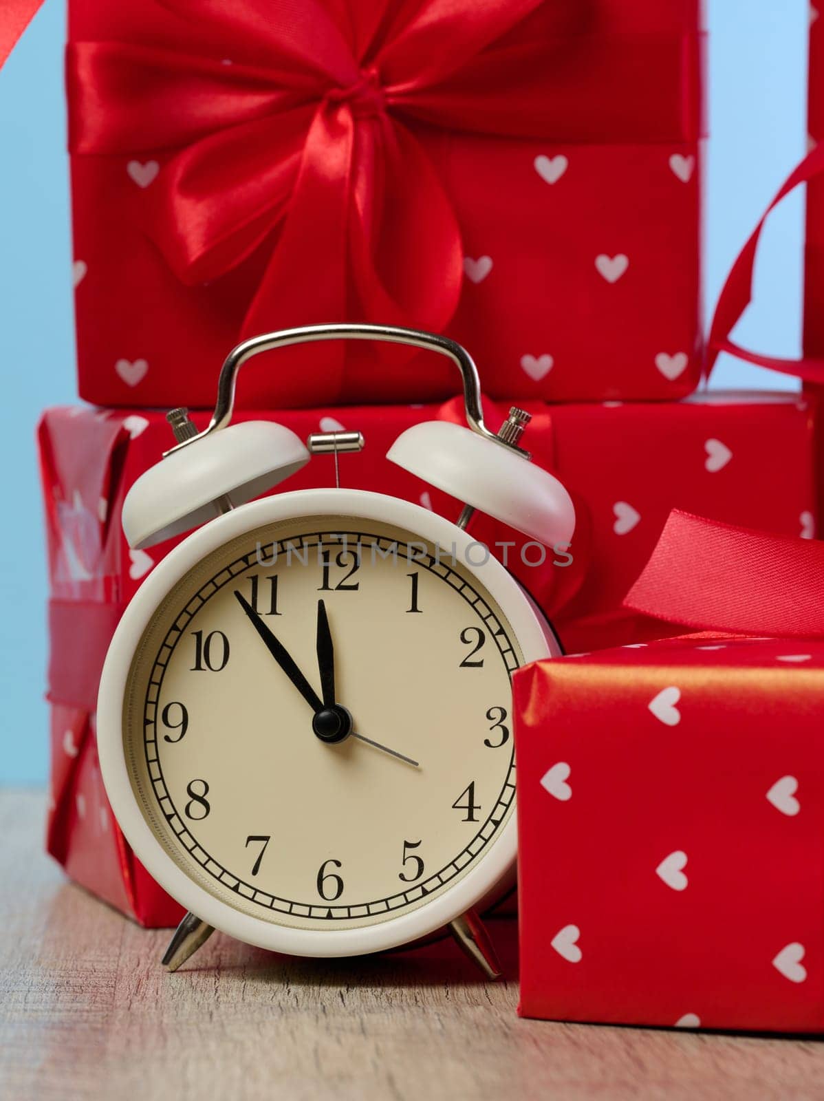 Alarm clock and stack of red gift boxes on blue background
