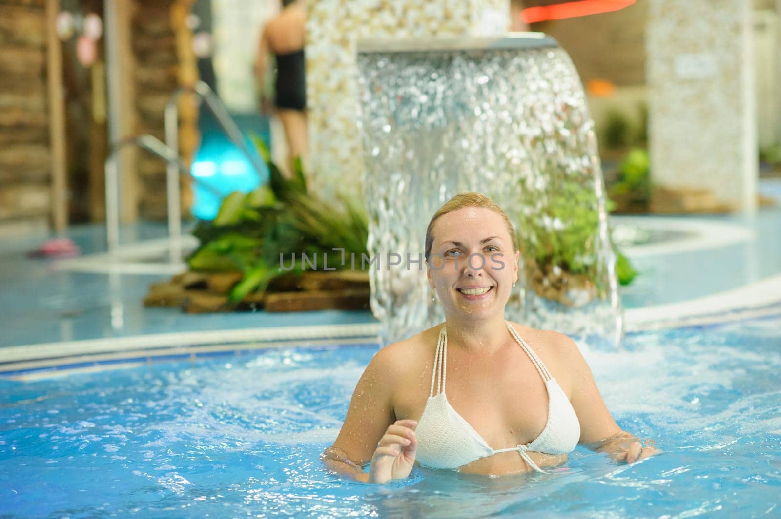 Woman enjoying the spray of the waterfall and relaxing in the pool by Lobachad