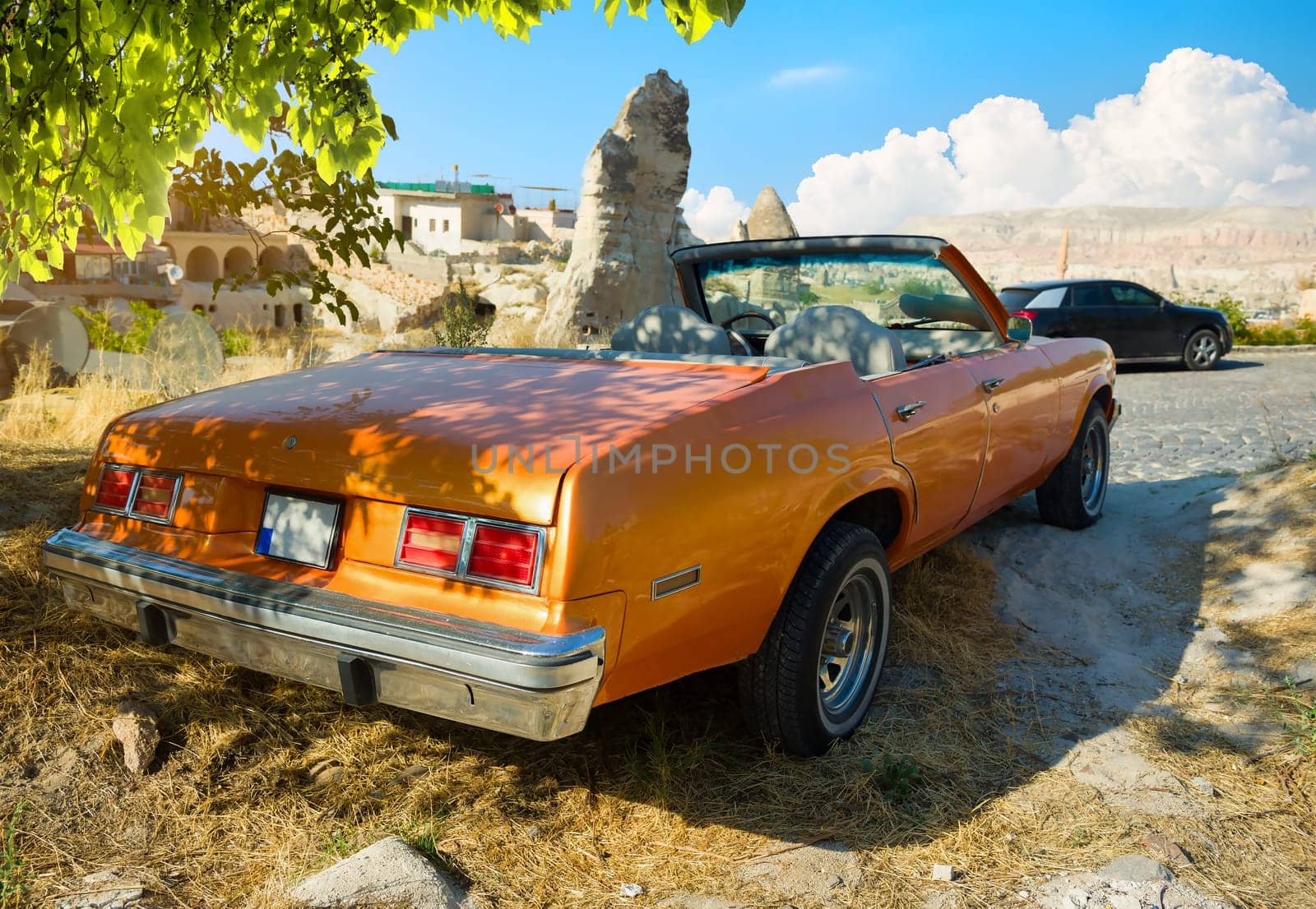 The orange retro car stands alone against the backdrop of a valley of hills