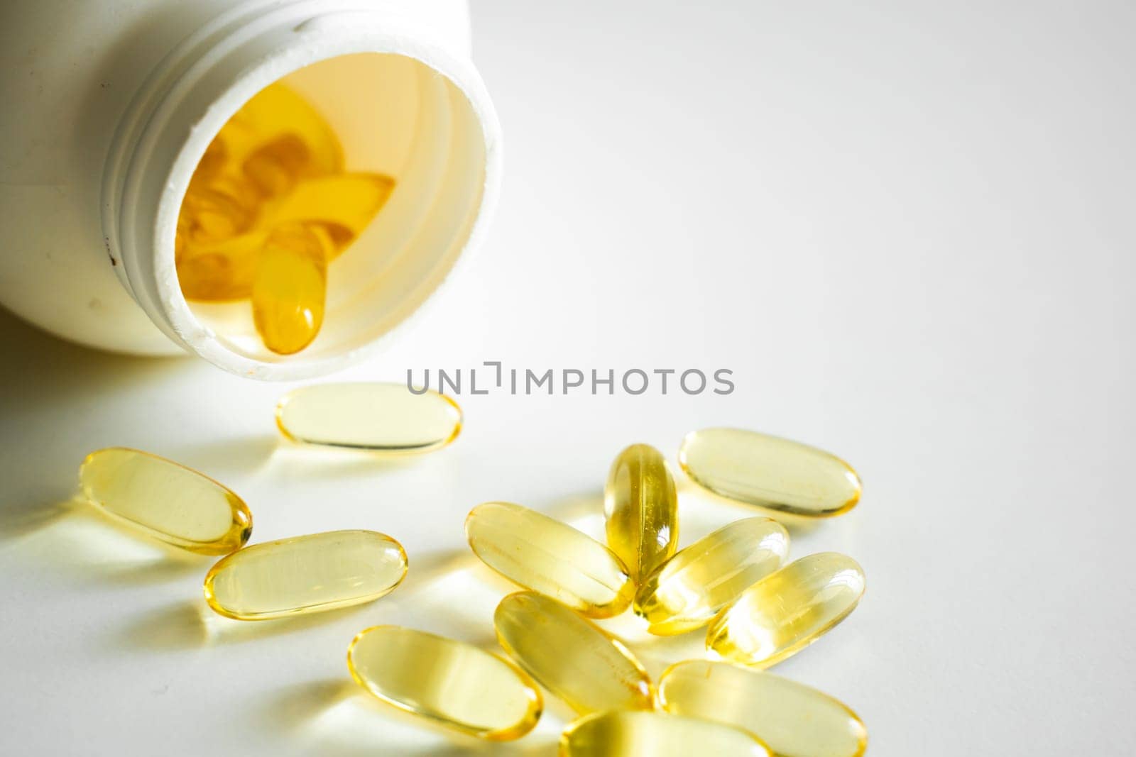 Open bottle with omega-3 capsules. Next to the lid with capsules. Medical concept. Pile of yellow softgel capsules Omega 3 fish oil scuttered from a white bottle bottle. Health care concept. by vovsht