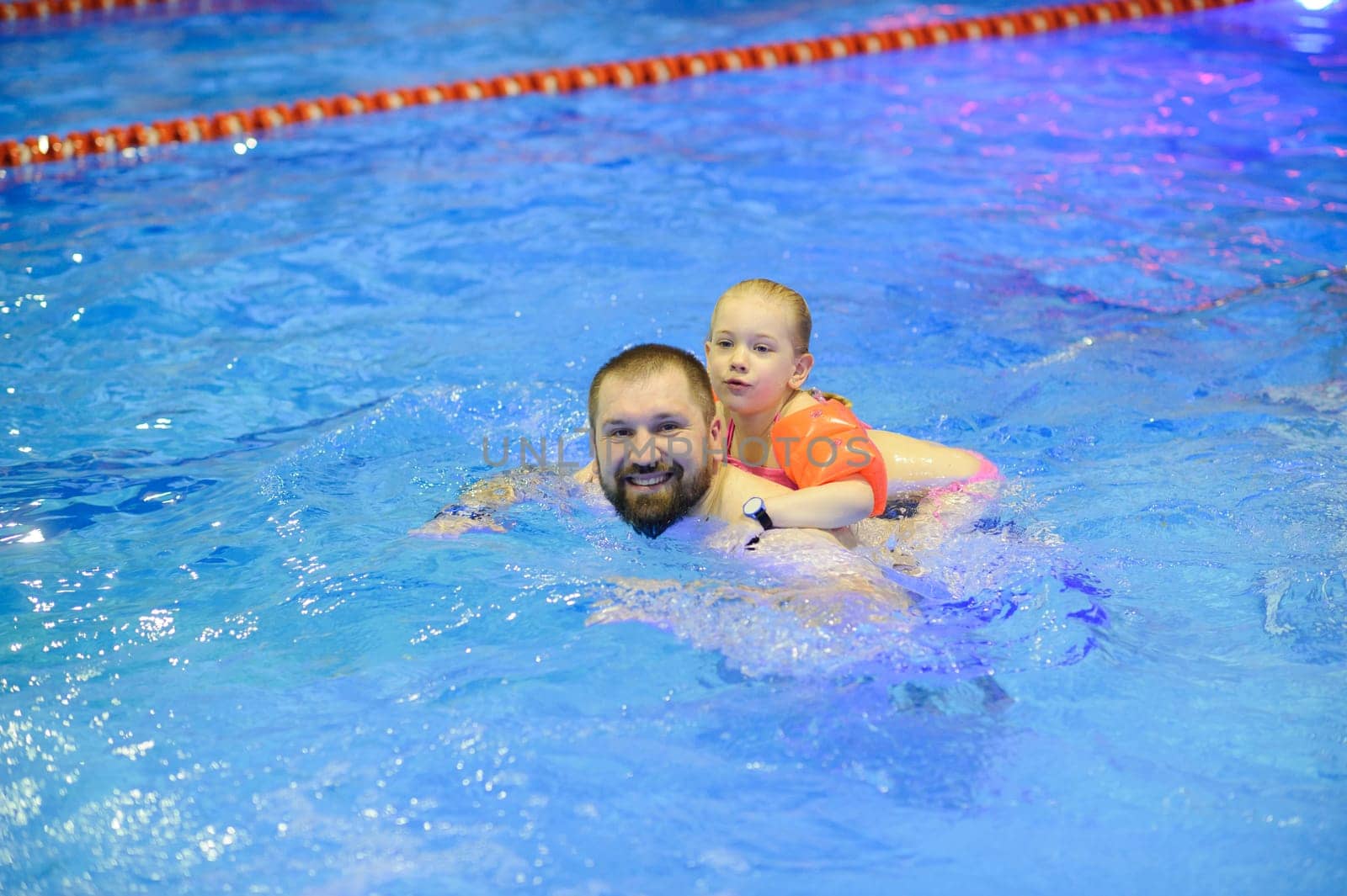 Dad and daughter are swimming in the pool with an inflatable. Healthy sports for the family.