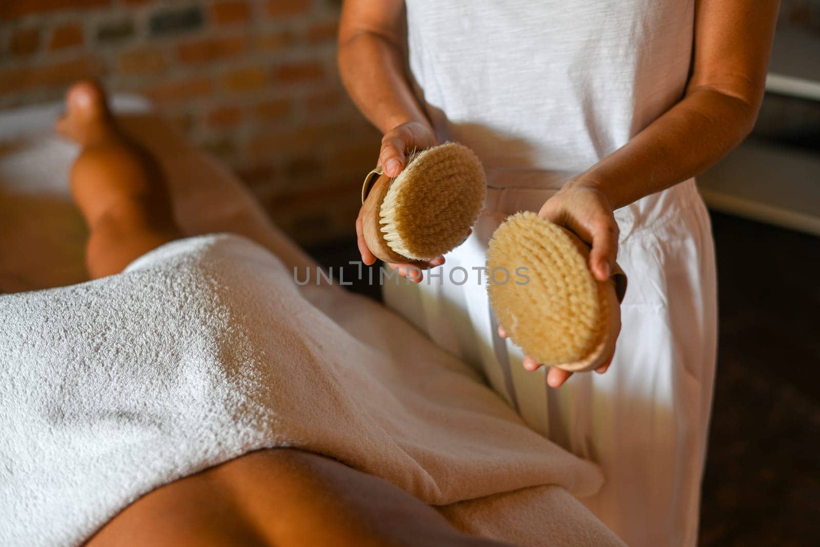 professional female physiotherapist masseuse performing brush massage to hispanic woman in spa clinic by verbano