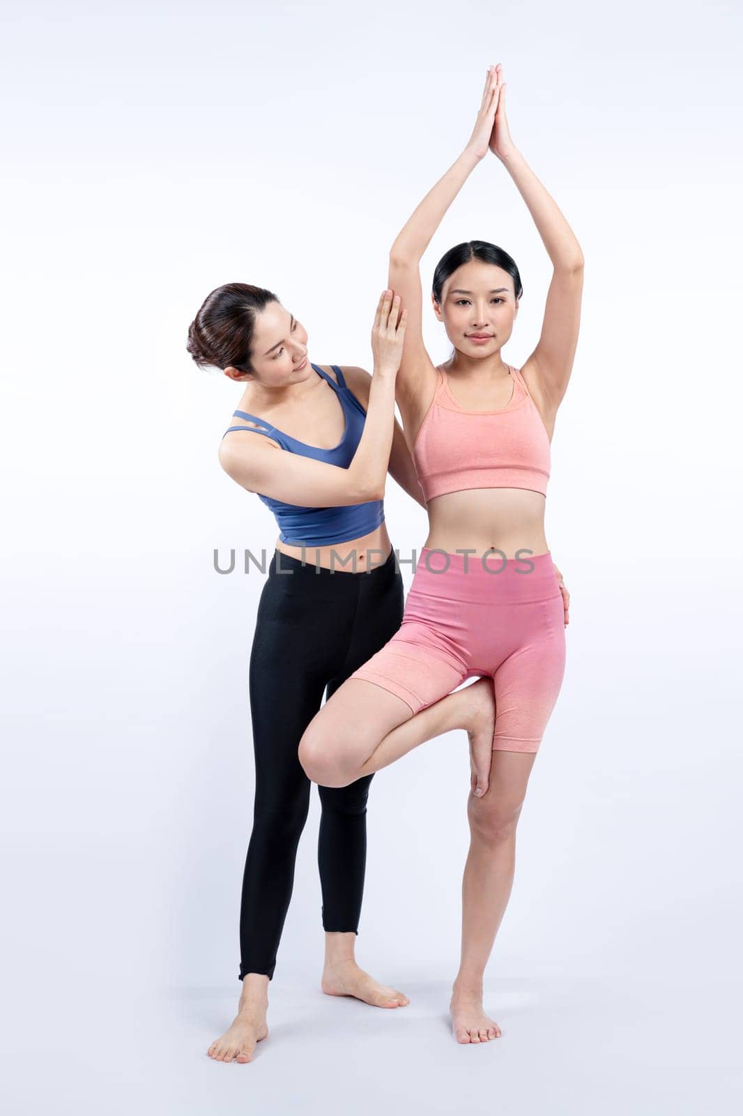 Asian woman in sportswear doing yoga exercise in standing pose with her trainer or yoga buddy. Healthy body care and meditation yoga lifestyle in full shot on isolated background. Vigorous