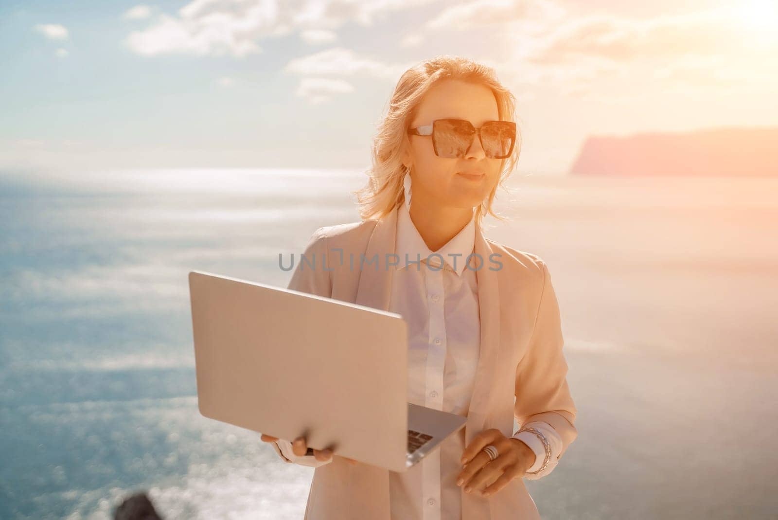 Freelance women sea. She is working on the computer. Good looking middle aged woman typing on a laptop keyboard outdoors with a beautiful sea view. The concept of remote work. by Matiunina