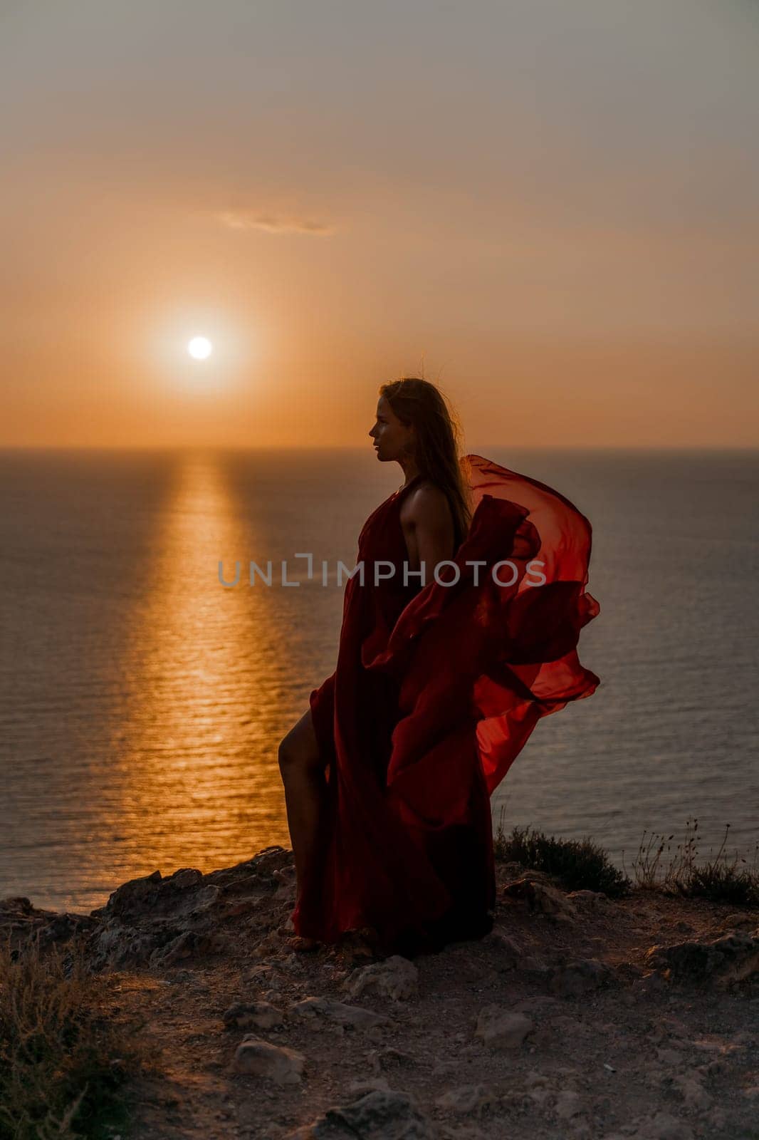 Woman sunset sea red dress, back view a happy beautiful sensual woman in a red long dress posing on a rock high above the sea on sunset. by Matiunina
