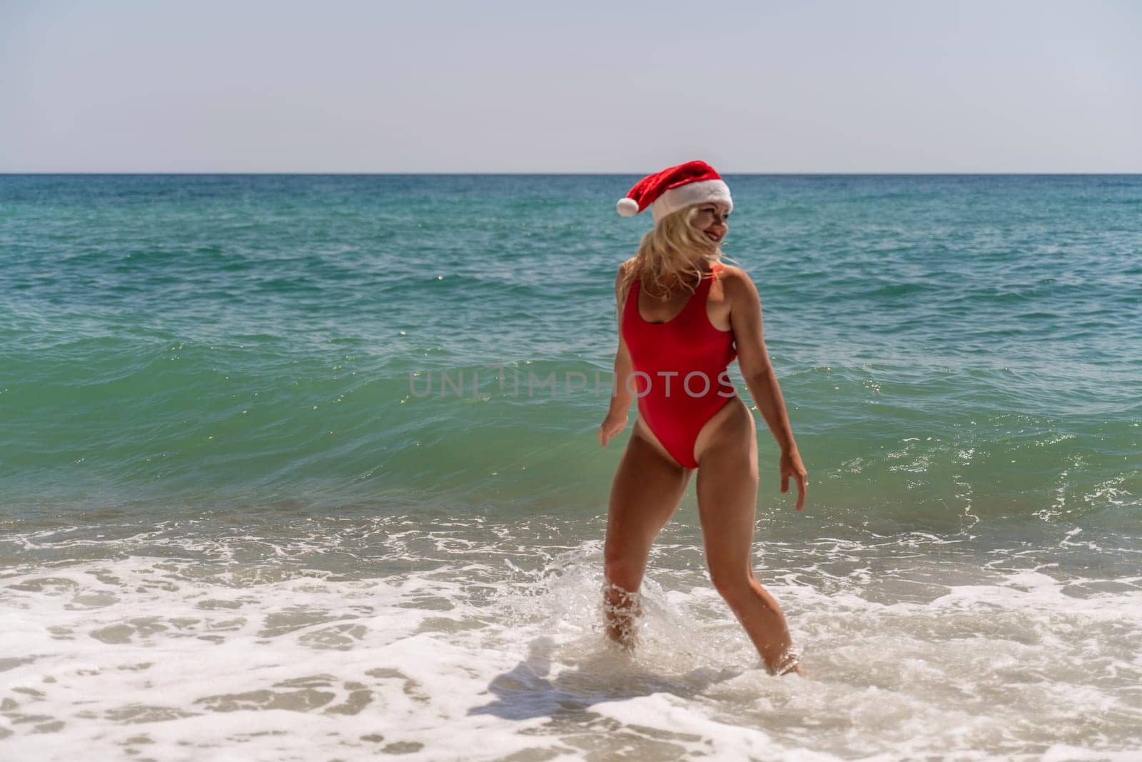 A woman in Santa hat on the seashore, dressed in a red swimsuit. New Year's celebration in a hot country.