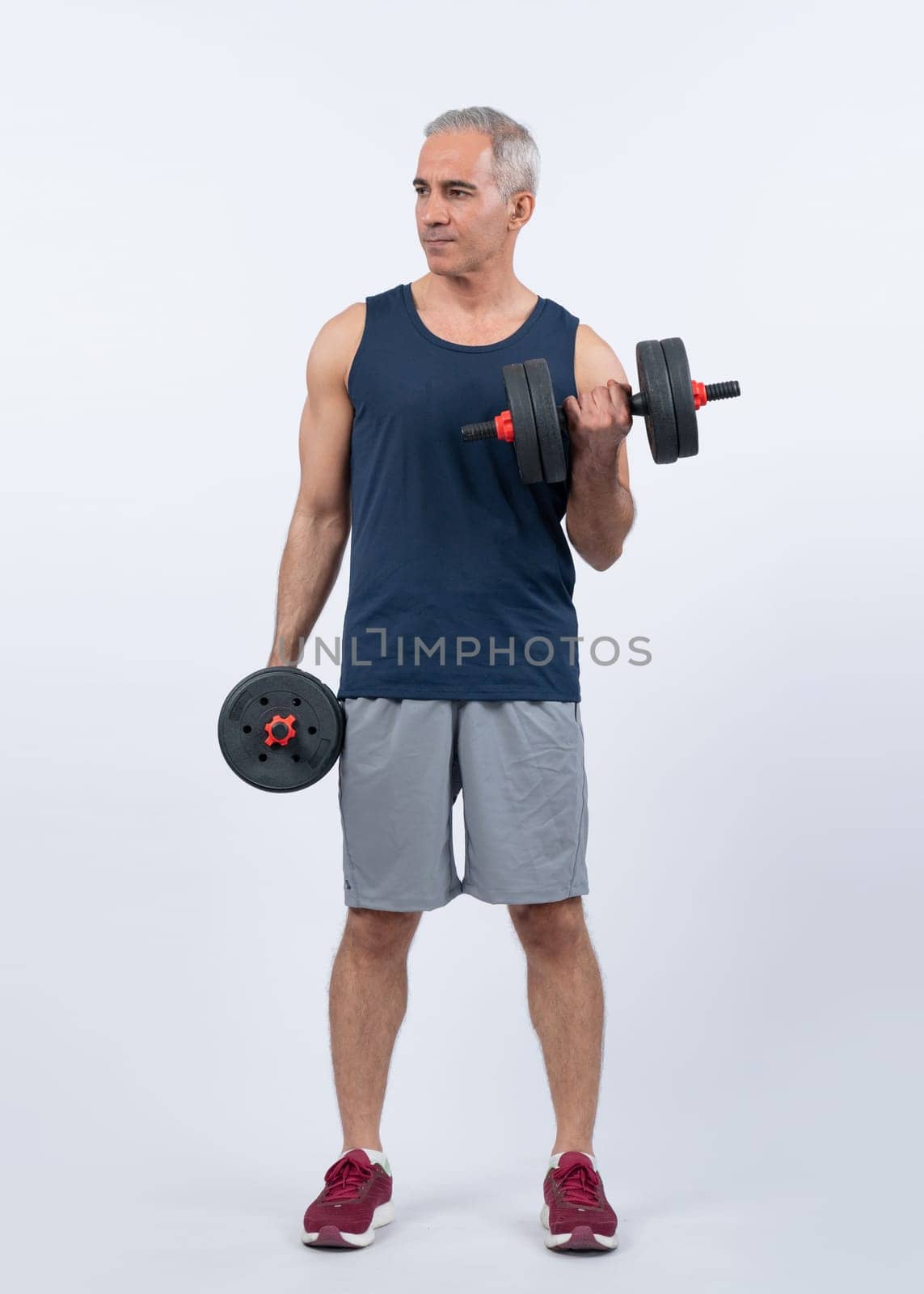 Full body length shot active and sporty senior man lifting dumbbell during weight training workout on isolated background. Healthy active physique and body care lifestyle for pensioner. Clout