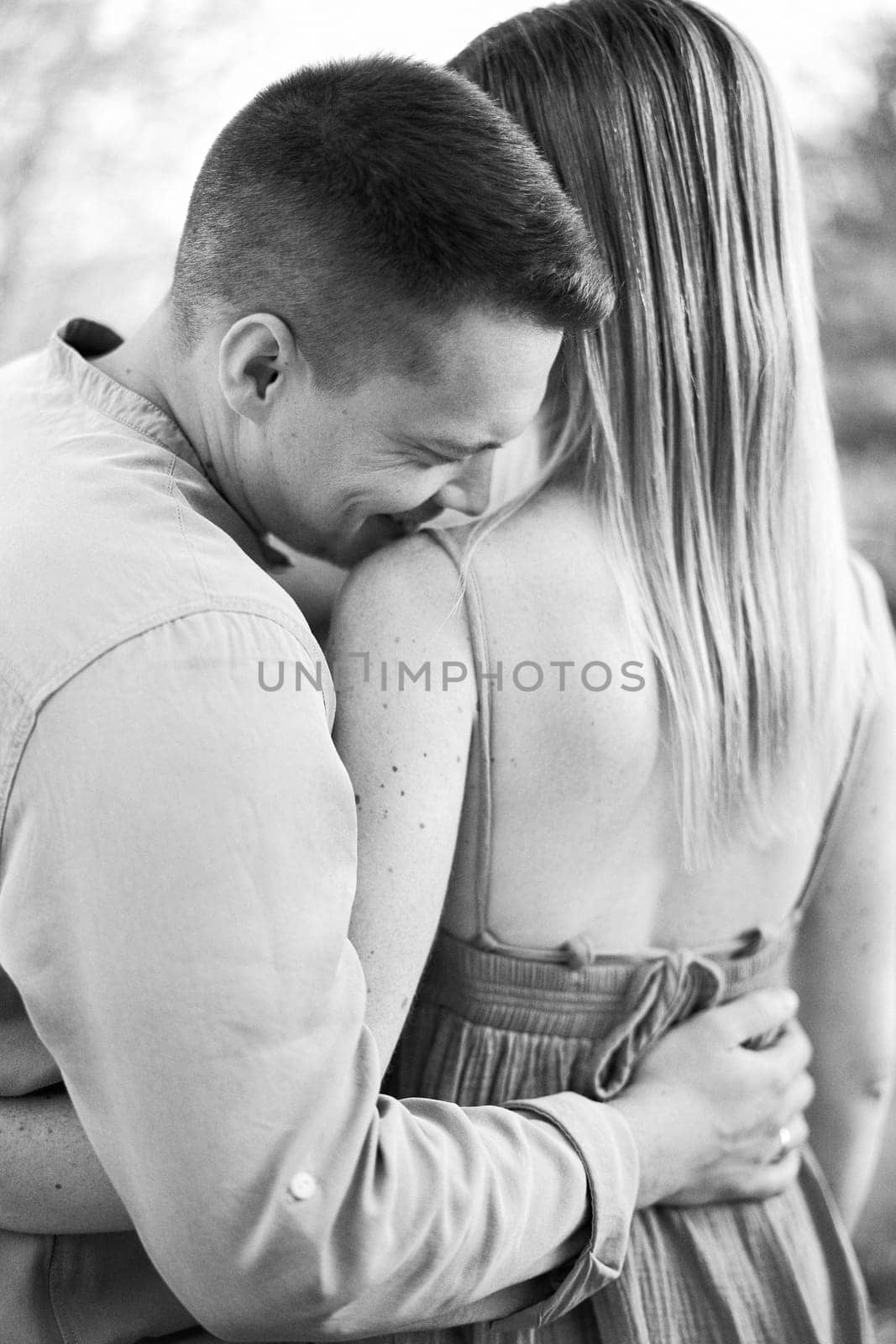 Smiling guy hugs girl by the waist and kisses her shoulder. Back view. Black and white photo. High quality photo