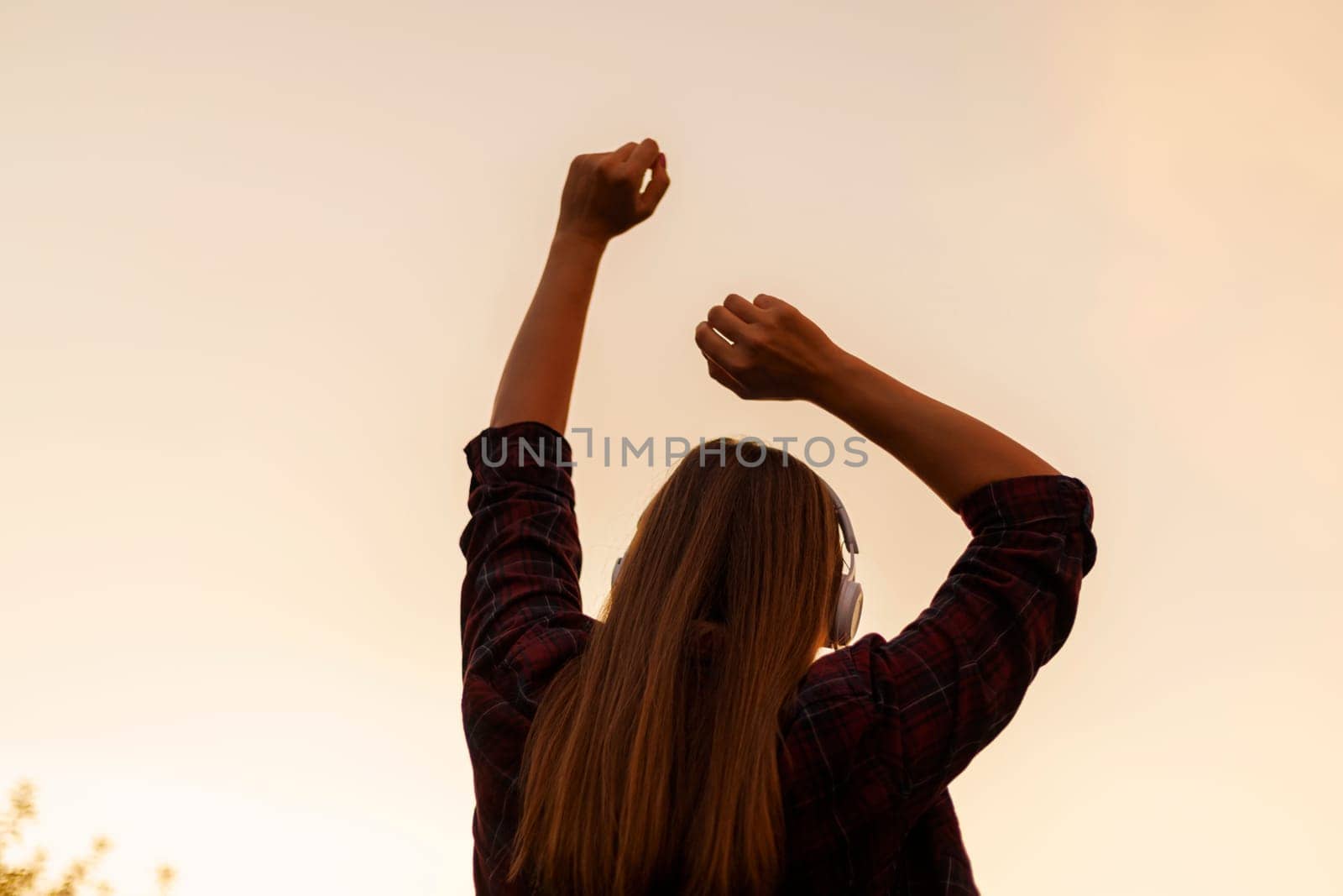 Silhouette of happy young woman in headphones enjoying music and dancing on a background of bright colorful sunset