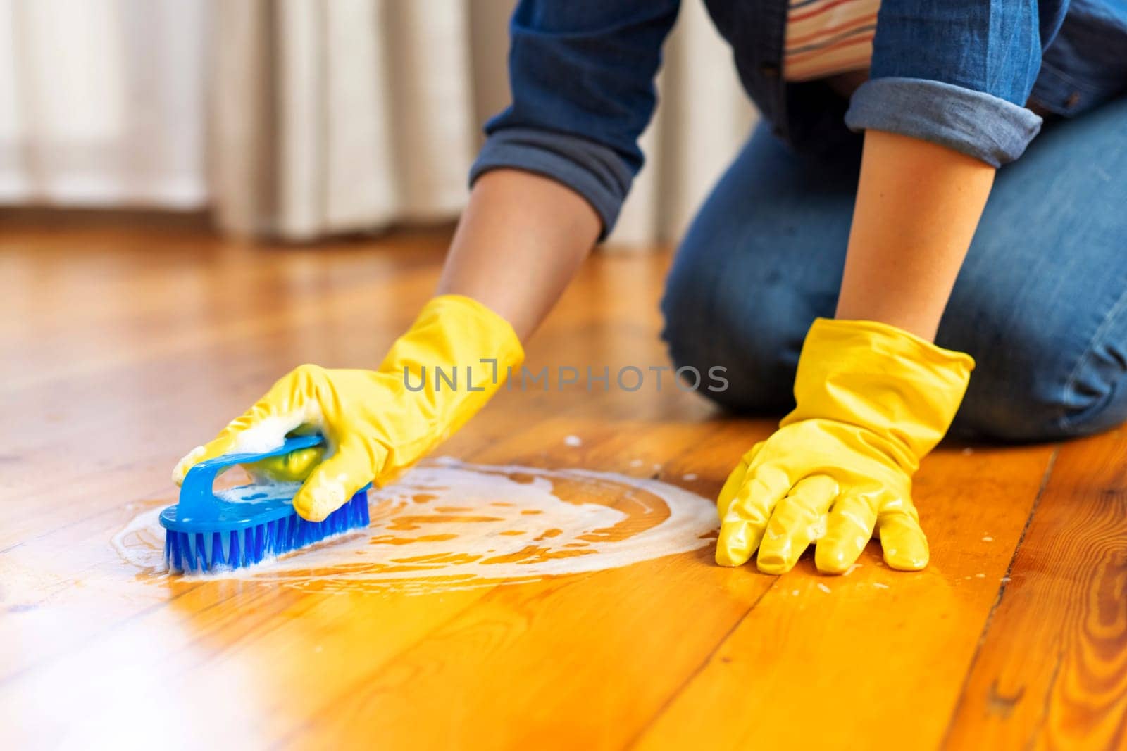 A young woman in protective gloves washes the floor with a brush and detergent by andreyz