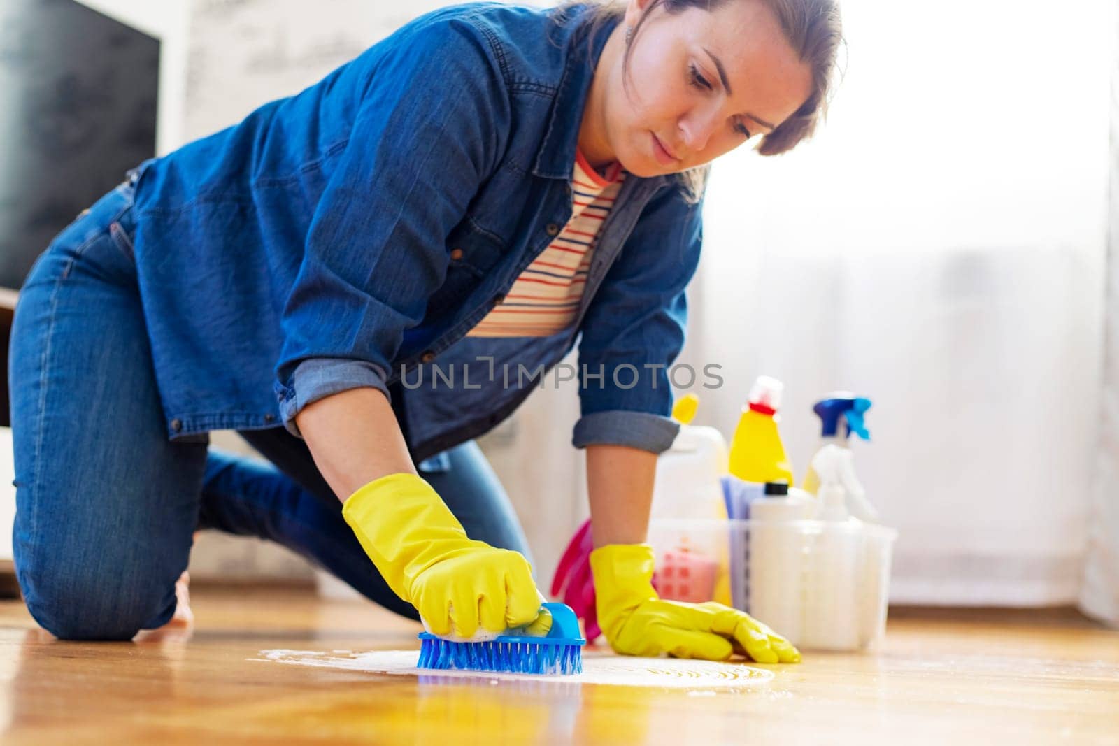 A young woman in protective gloves washes the floor with a brush and detergent by andreyz