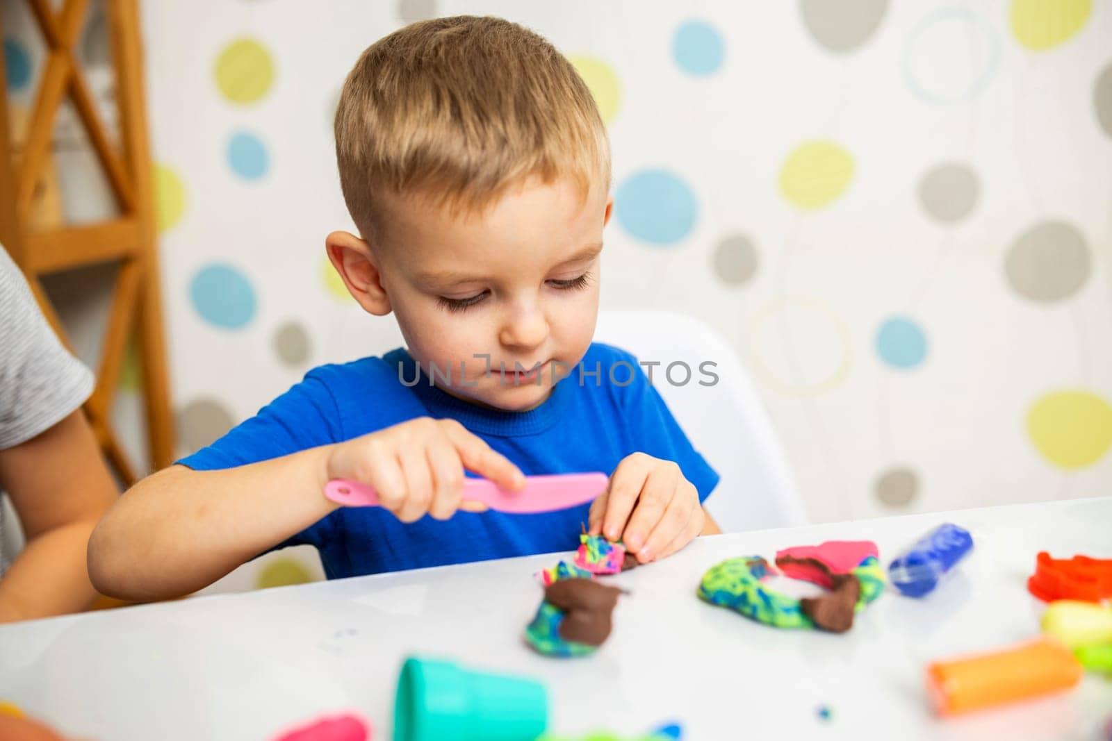 Little boy enthusiastically plays with plasticine, play dough on white table at home, children's creativity concept. Development of fine motor skills