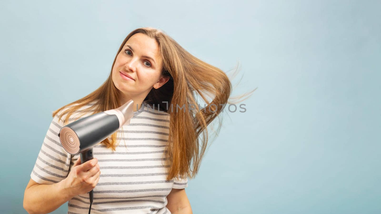 Beautiful young woman using hair dryer on light blue background by andreyz