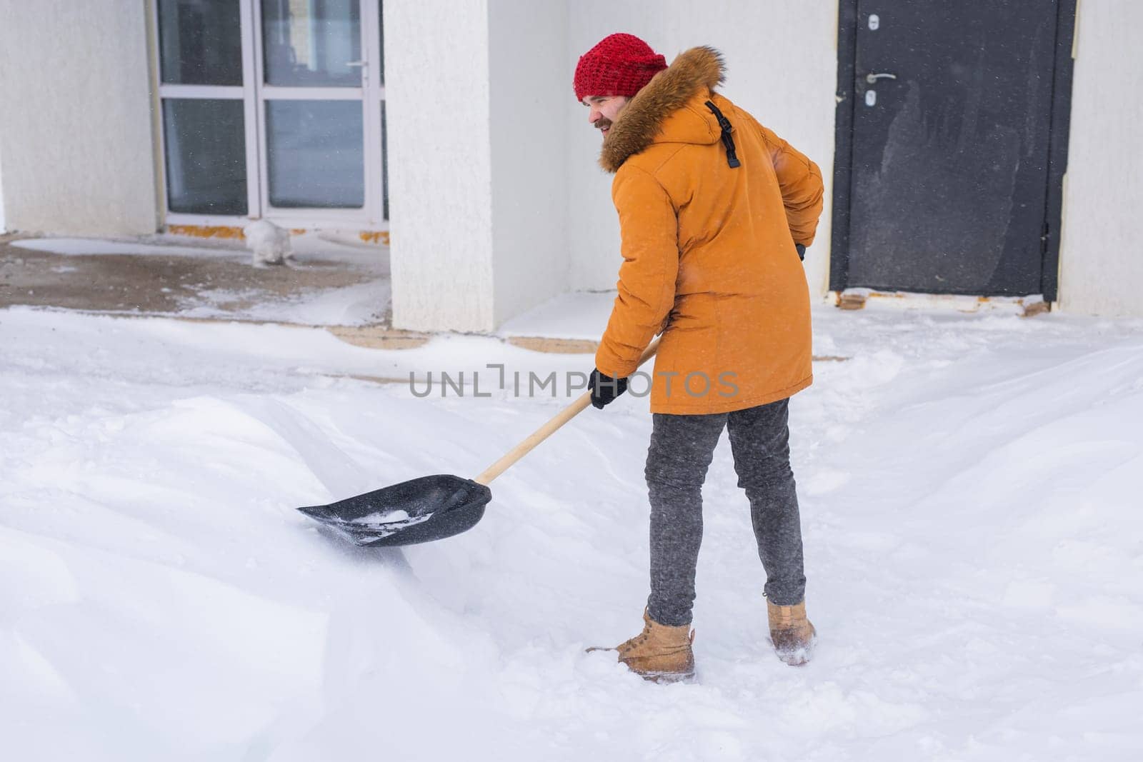 A man cleans and clears the snow in front of the house on frosty day. Cleaning the street from snow on a winter day. Snowfall and severe snowstorm in winter