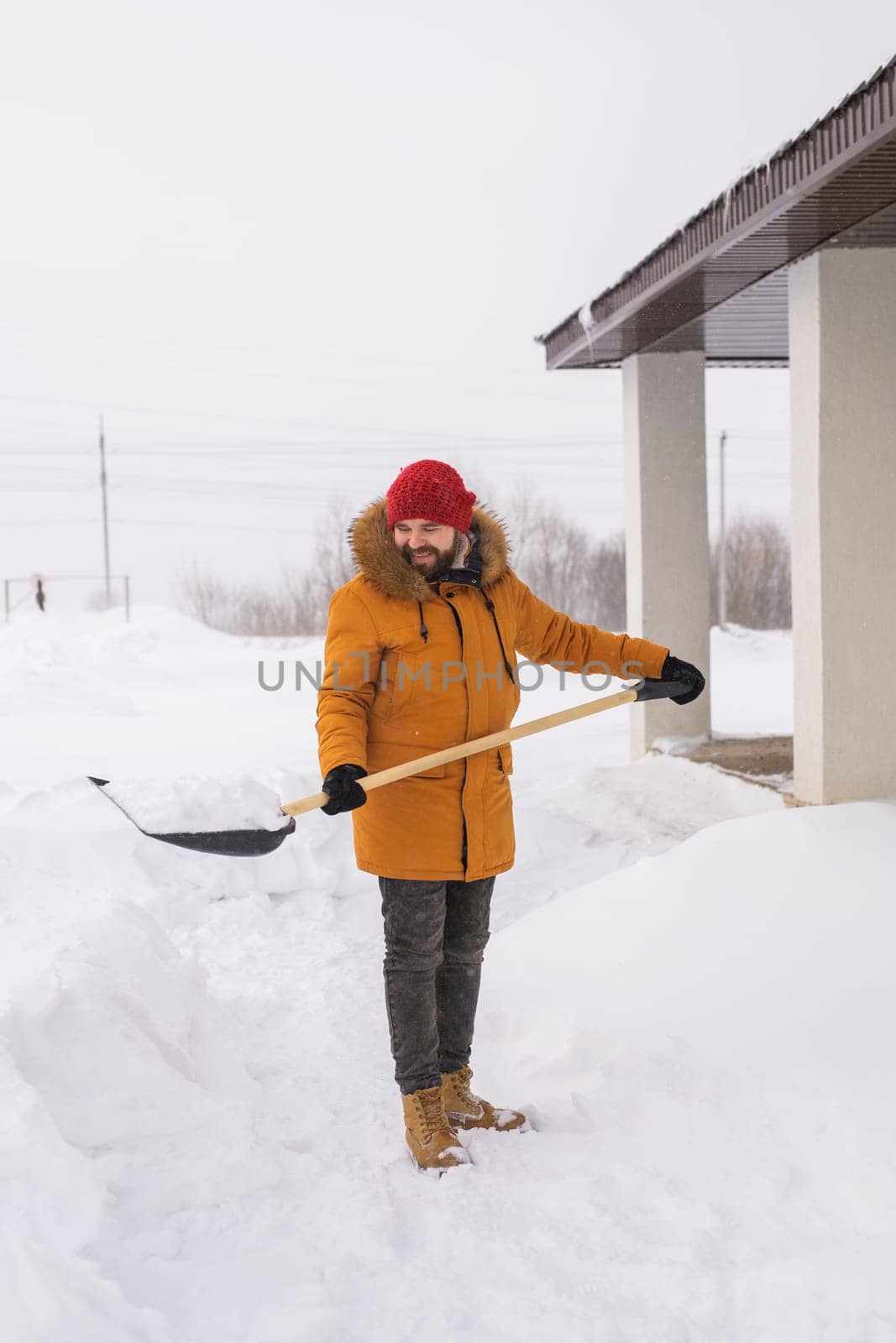 A man cleans and clears the snow in front of the house on frosty day. Cleaning the street from snow on a winter day. Snowfall and severe snowstorm in winter. by Satura86