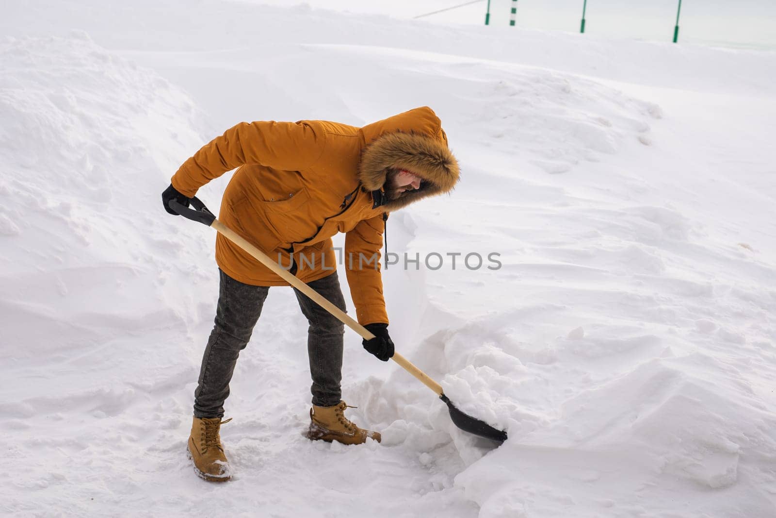 A man cleans and clears the snow in front of the house on frosty day. Cleaning the street from snow on a winter day. Snowfall and severe snowstorm in winter