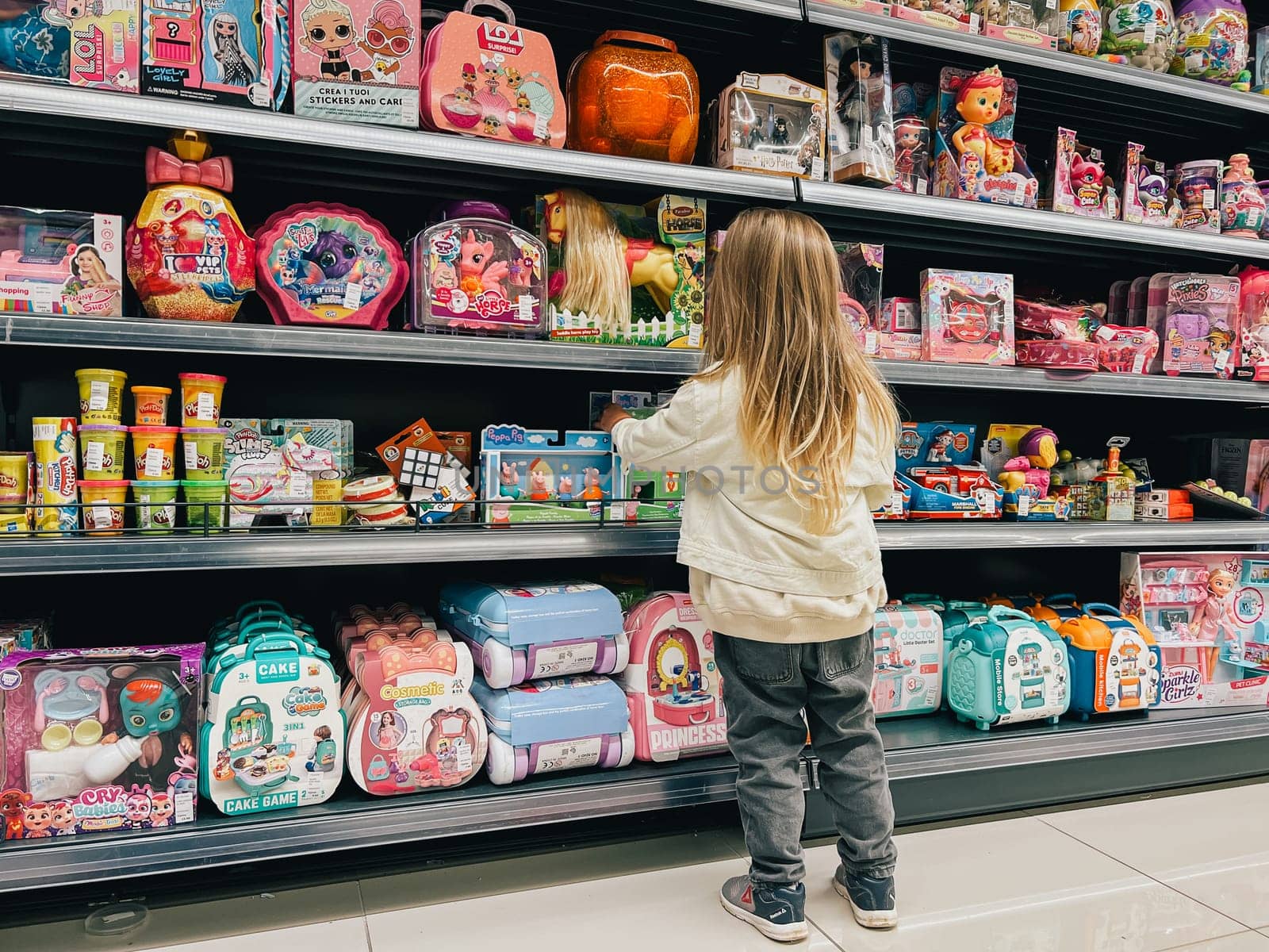 Little girl stands in front of the shelves with toys in the supermarket. High quality photo